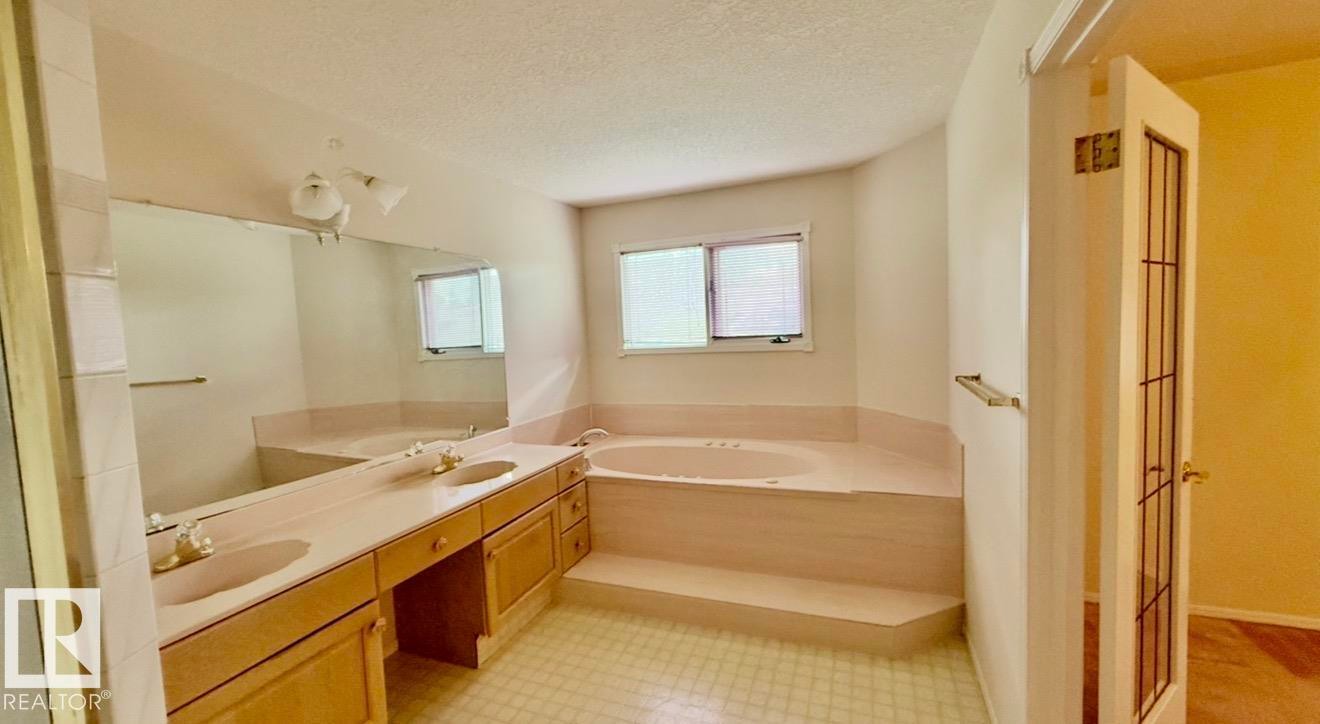 Bathroom featuring a double vanity with light wood cabinetry, dual sinks, and a large wall-mounted mirror - 134 Wolf Ridge Place, Edmonton, AB
