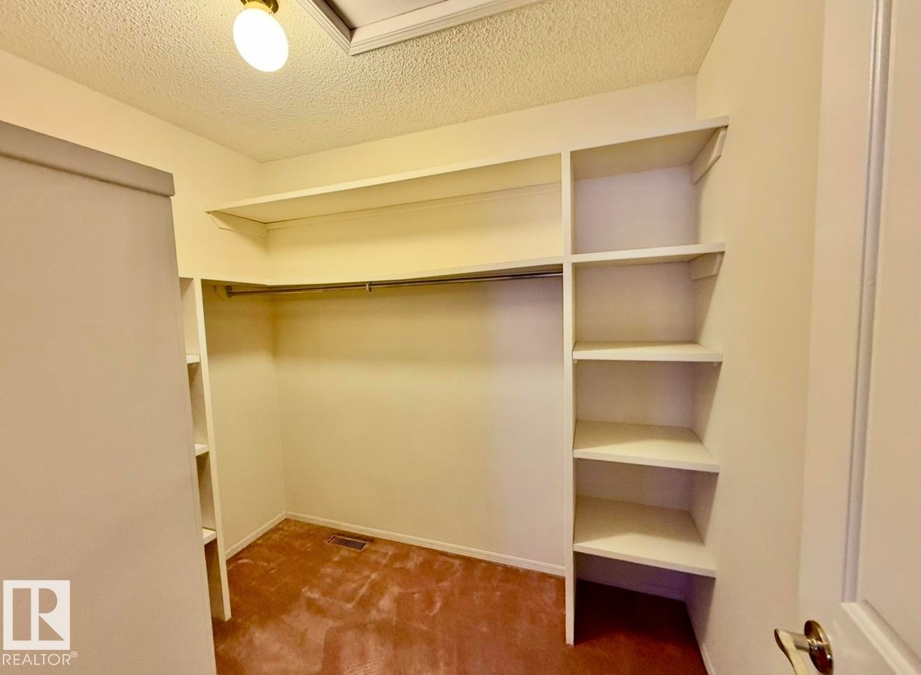 Walk-in closet featuring built-in shelving, hanging rod, textured ceiling, and flush-mount lighting - 134 Wolf Ridge Place, Edmonton, AB