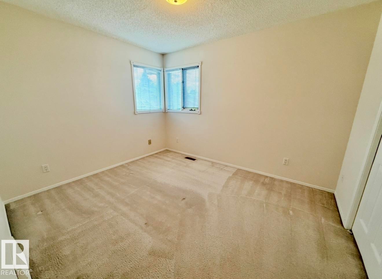 Room featuring a corner window with horizontal blinds, neutral wall paint, and light-colored carpeting - 134 Wolf Ridge Place, Edmonton, AB