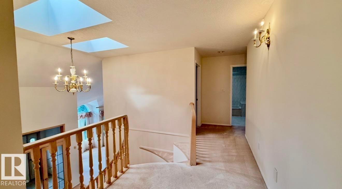 Upper-level landing featuring a carpeted floor, two skylights, a chandelier, and a wood banister - 134 Wolf Ridge Place, Edmonton, AB