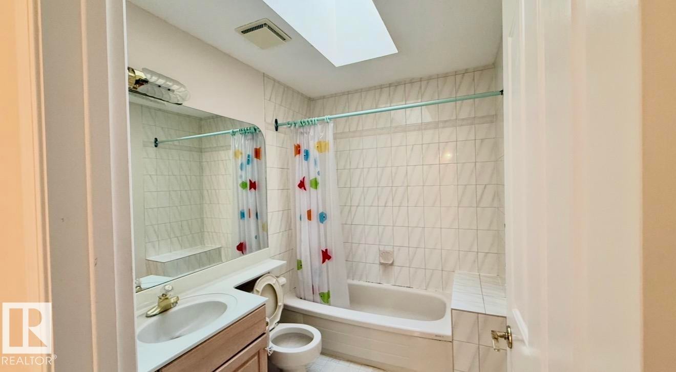 Bathroom featuring a white bathtub, ceramic tile shower surround, single vanity, and skylight - 134 Wolf Ridge Place, Edmonton, AB