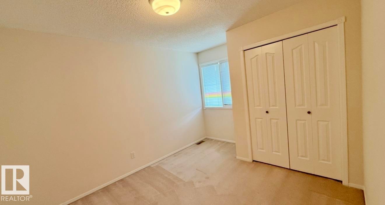 Neutral-toned room featuring a window with horizontal blinds, bi-fold closet doors, wall-to-wall carpeting, and a flush-mount ceiling light fixture - 134 Wolf Ridge Place, Edmonton, AB