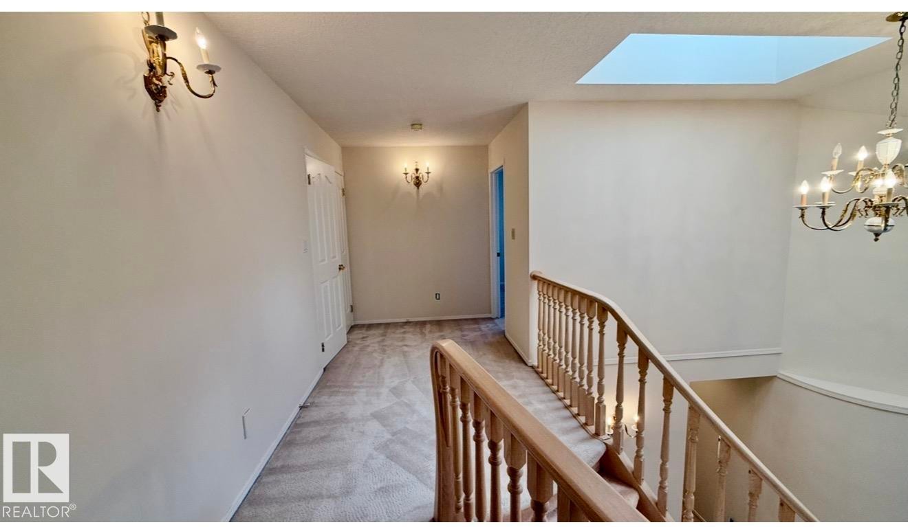 Carpeted hallway with a central skylight, wood-finish stair railing, and multiple wall sconces providing ambient lighting - 134 Wolf Ridge Place, Edmonton, AB