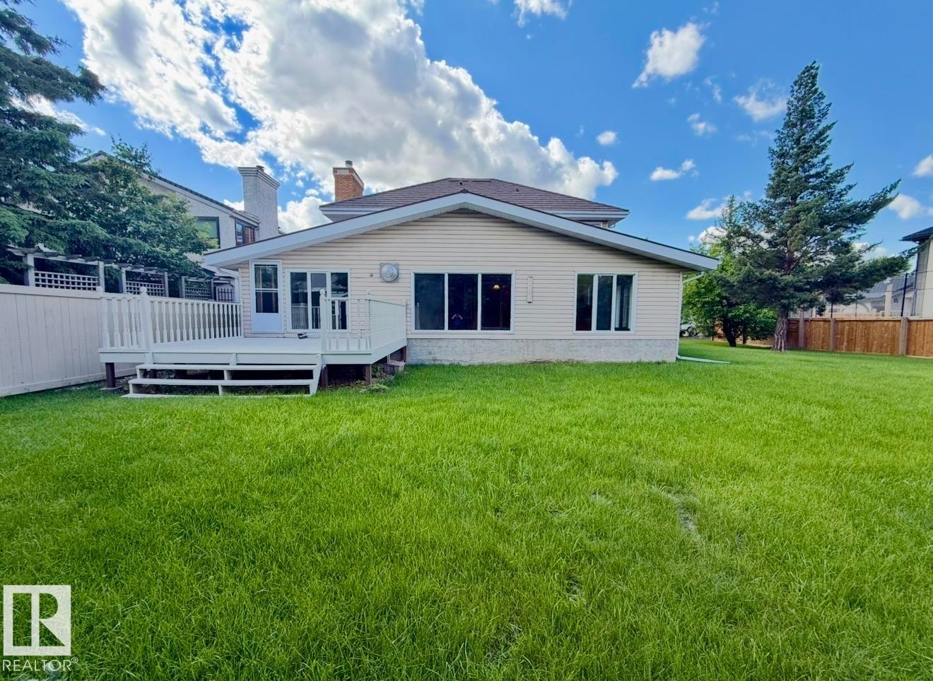 Spacious rear yard with a large deck, white privacy fence, and mature trees - 134 Wolf Ridge Place, Edmonton, AB