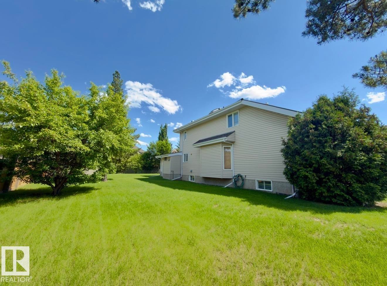 Expansive backyard featuring a manicured lawn, mature trees, and natural landscaping - 134 Wolf Ridge Place, Edmonton, AB