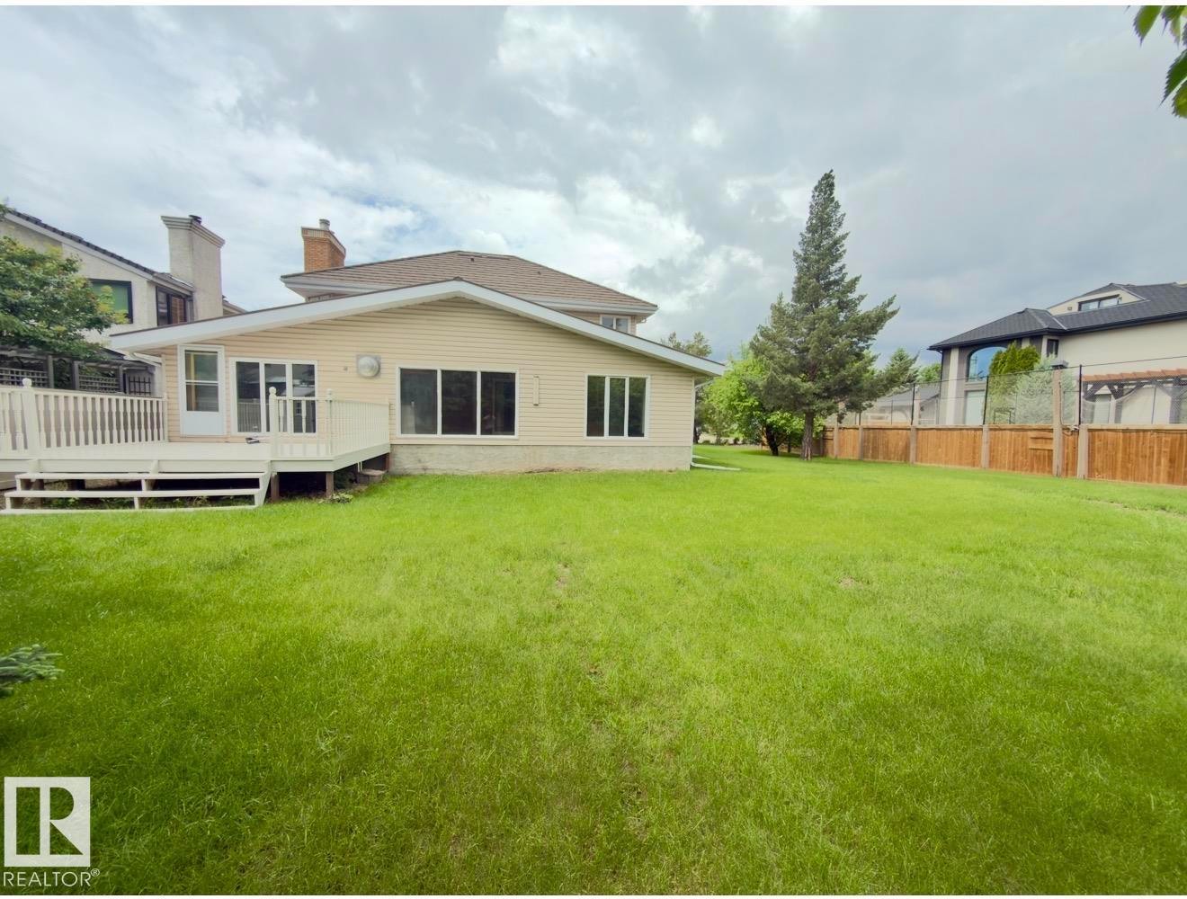 Expansive backyard featuring a large green lawn, a white wooden deck with railing, and multiple windows - 134 Wolf Ridge Place, Edmonton, AB