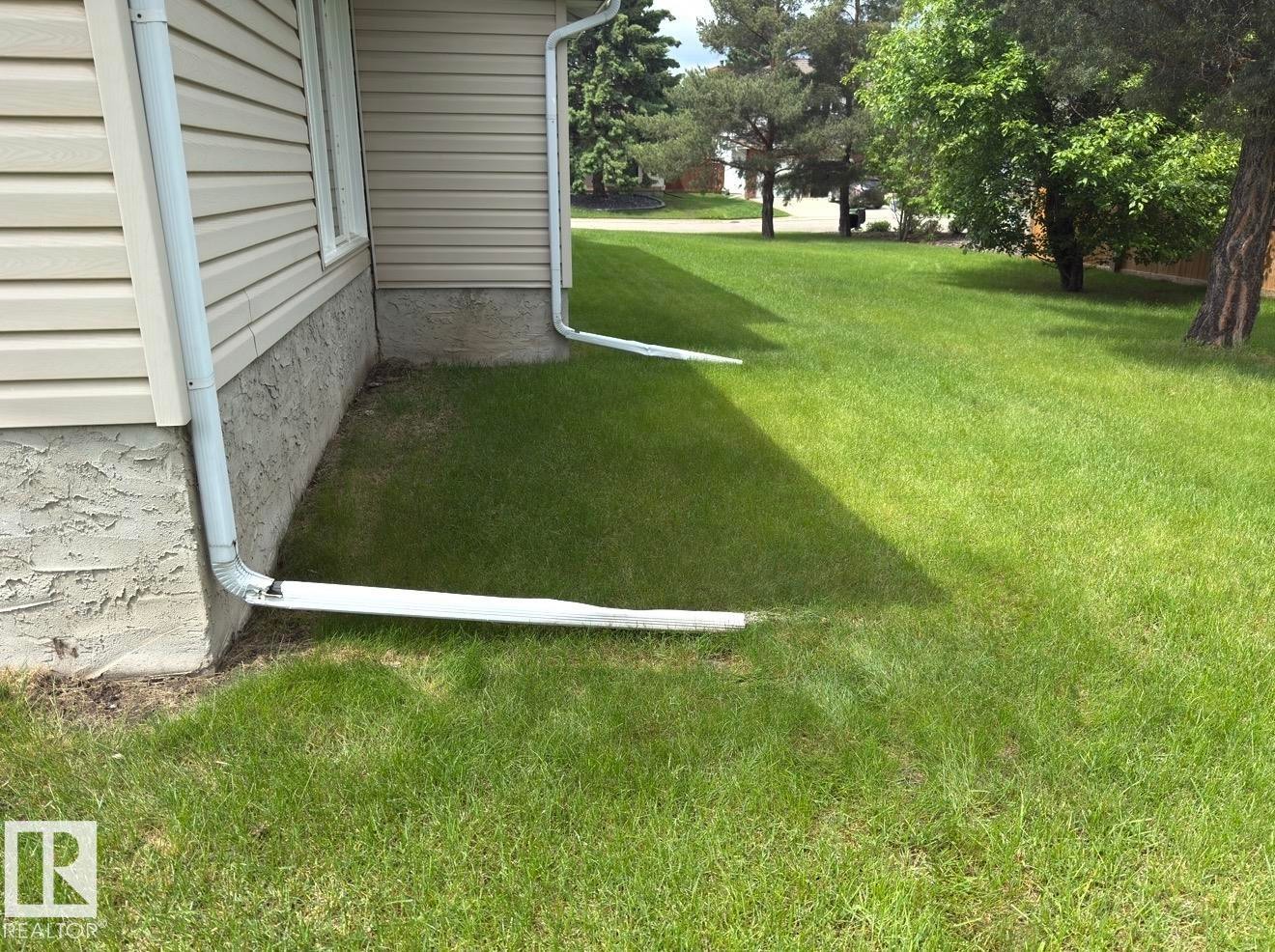 Exterior siding in a neutral tone with white downspouts, featuring a textured foundation and a verdant lawn - 134 Wolf Ridge Place, Edmonton, AB