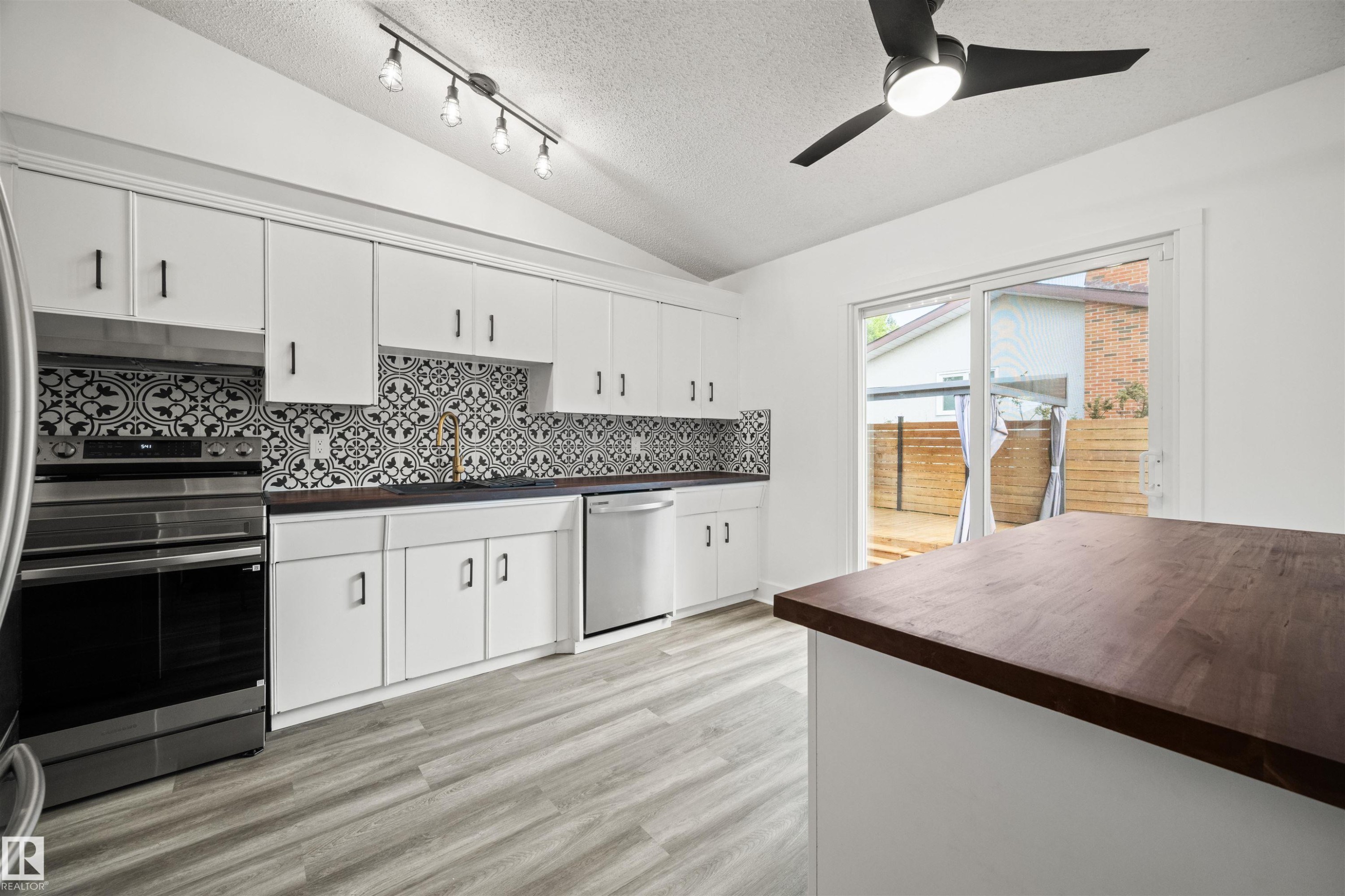 Kitchen featuring white cabinetry, patterned tile backsplash, wood-finish countertops, stainless steel appliances, and light wood-finish flooring - 28 Goodridge Drive, St. Albert, AB