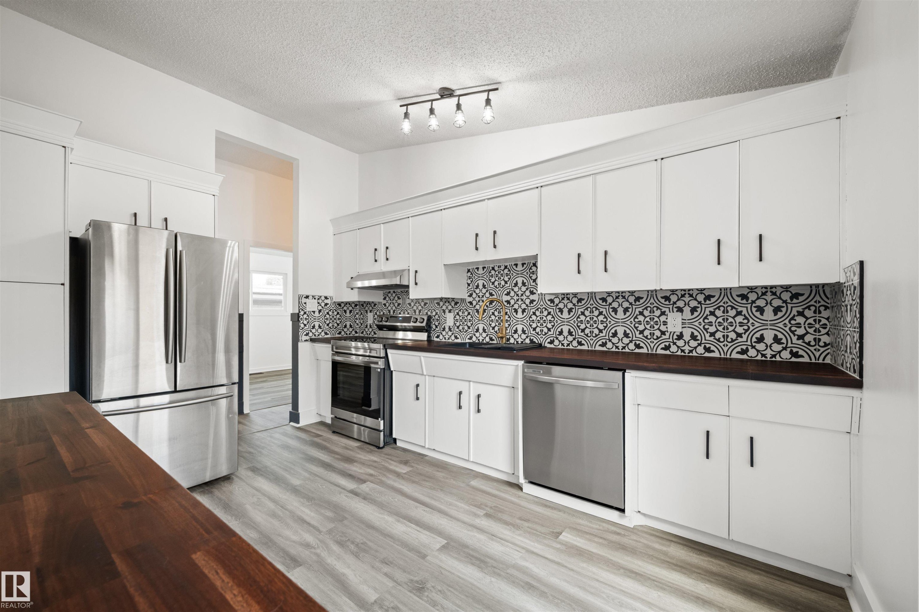 Bright kitchen featuring wood-finish flooring, white cabinetry with black hardware, dark wood-finish countertops, and a patterned tile backsplash - 28 Goodridge Drive, St. Albert, AB