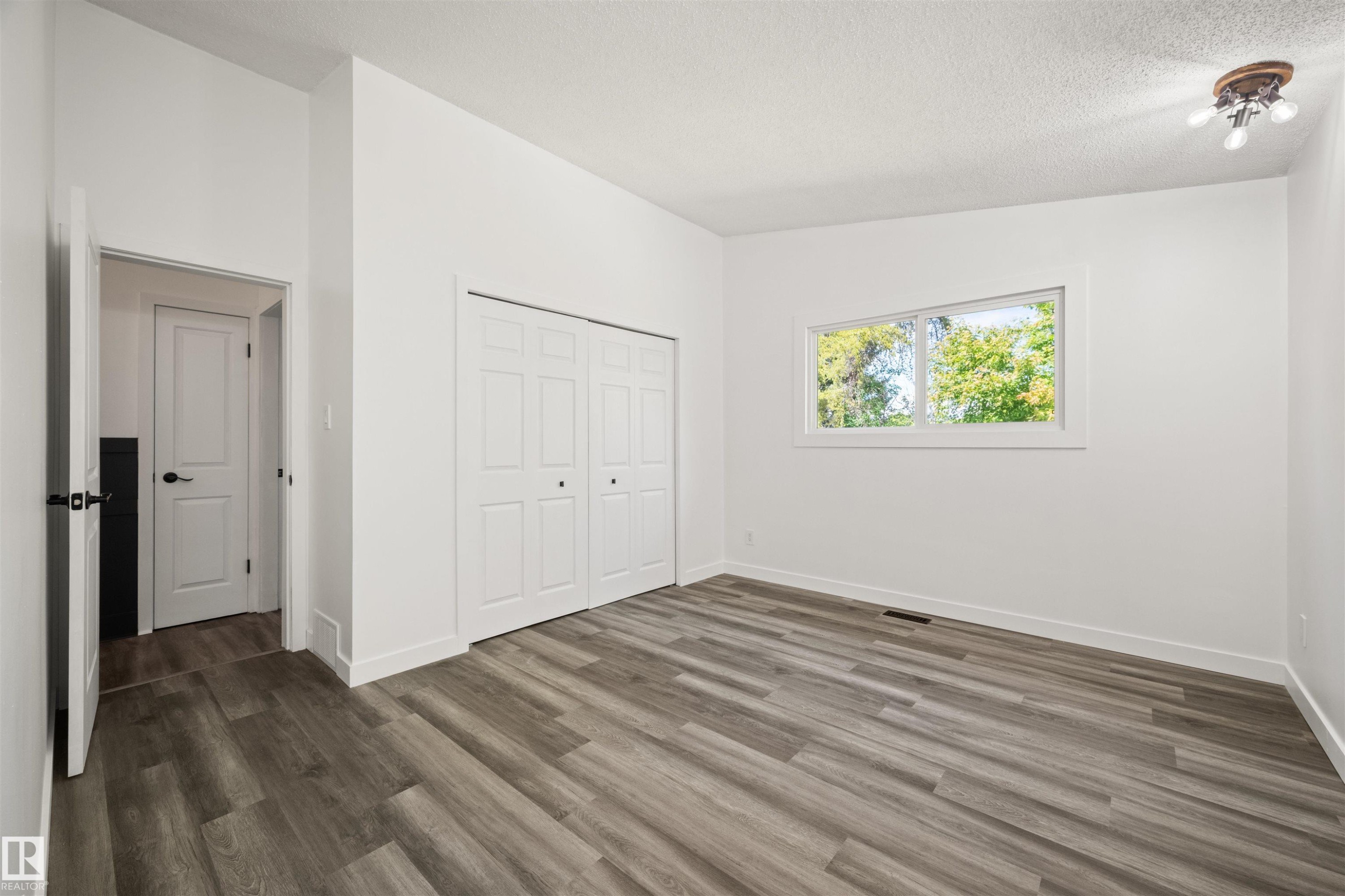 Spacious room featuring wood-finish flooring, white walls, and a large window - 28 Goodridge Drive, St. Albert, AB