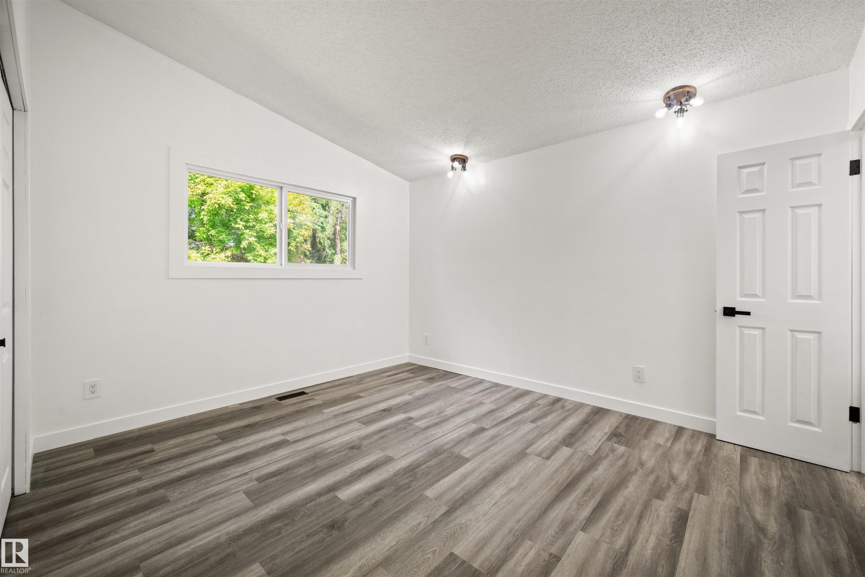 Spacious room featuring wood-finish flooring, crisp white walls, and a large window - 28 Goodridge Drive, St. Albert, AB