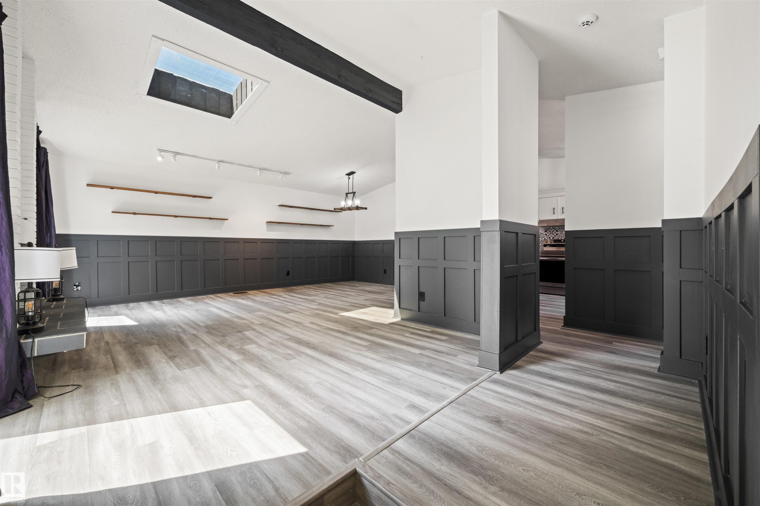 Spacious room featuring wood-finish flooring, wainscoting, a skylight, exposed beam, and track lighting - 28 Goodridge Drive, St. Albert, AB