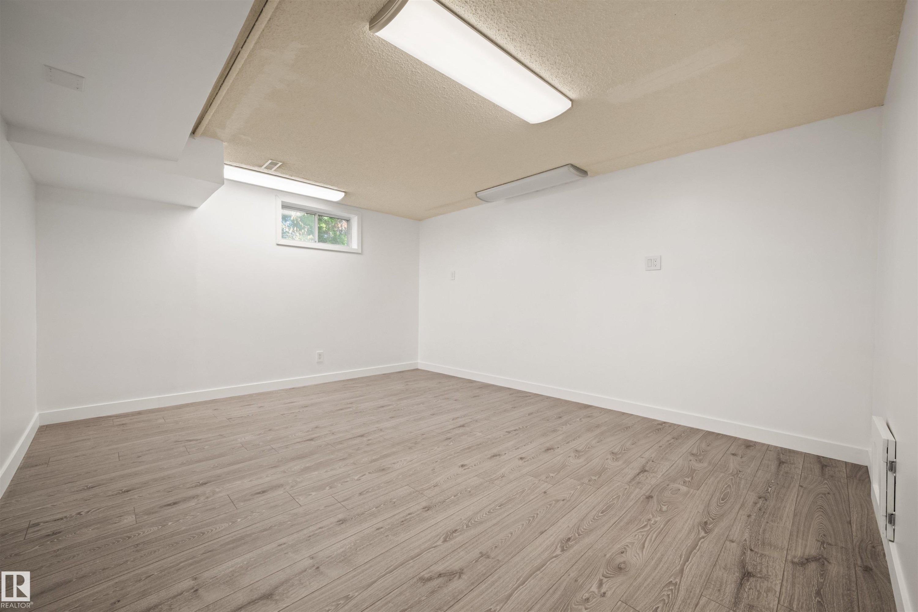 Spacious room featuring light wood-finish flooring, white painted walls, and a textured ceiling with flush-mount lighting fixtures - 28 Goodridge Drive, St. Albert, AB