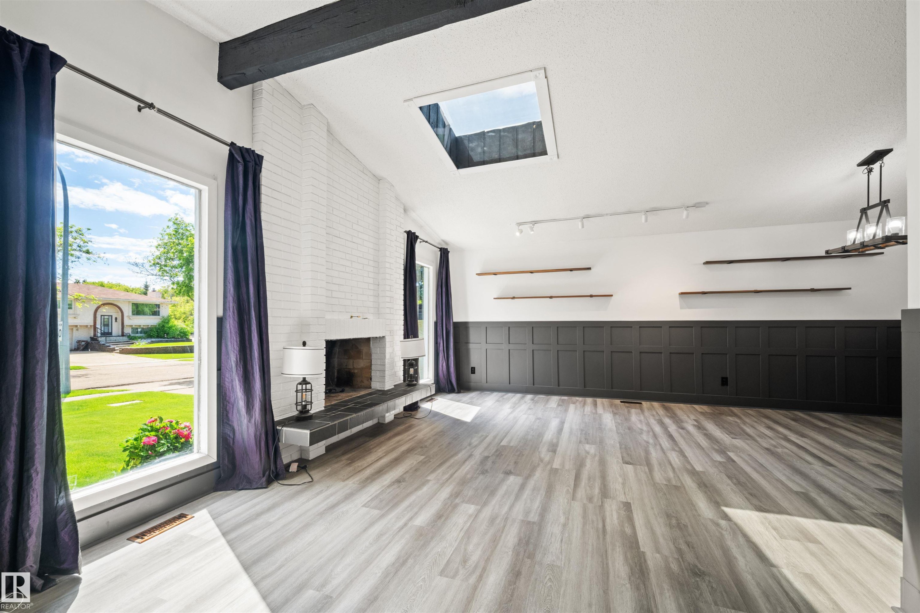 Spacious room featuring light wood-finish flooring and a white brick fireplace with a dark tile hearth - 28 Goodridge Drive, St. Albert, AB