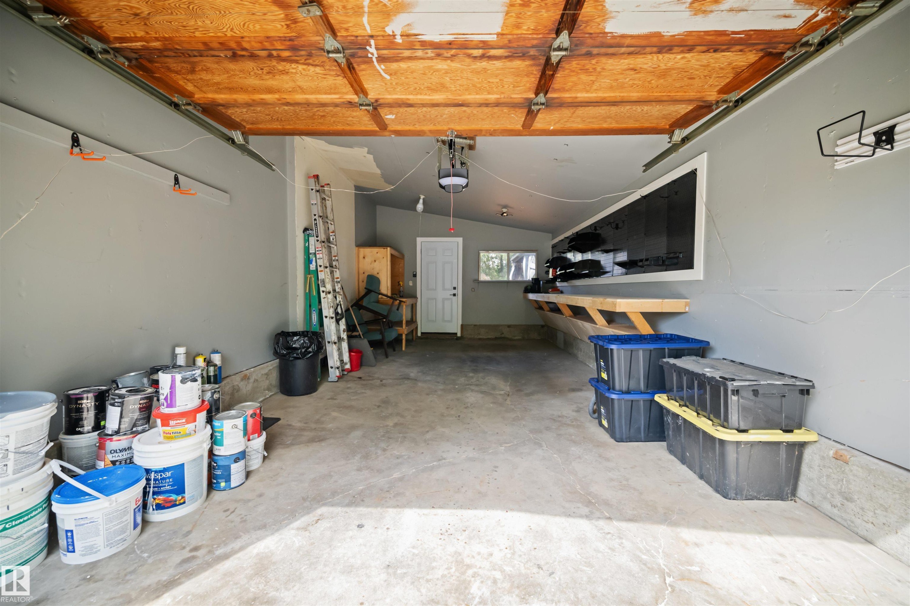 Attached two-car garage with concrete flooring, integrated workbench, and overhead garage door mechanism - 28 Goodridge Drive, St. Albert, AB