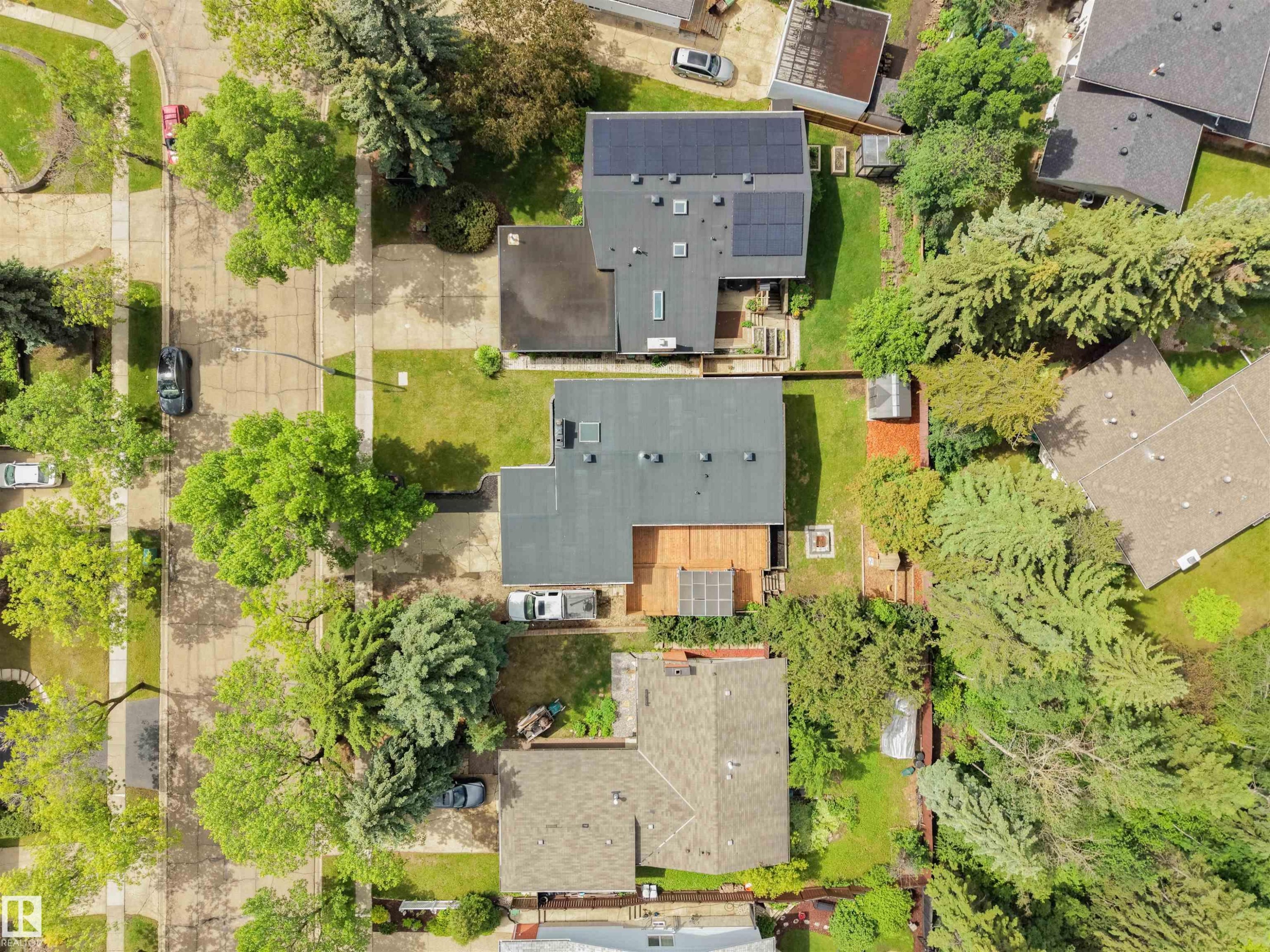 Aerial view showcasing two residential properties featuring mature landscaping, a private wooden deck, and a solar panel system on one roof - 28 Goodridge Drive, St. Albert, AB
