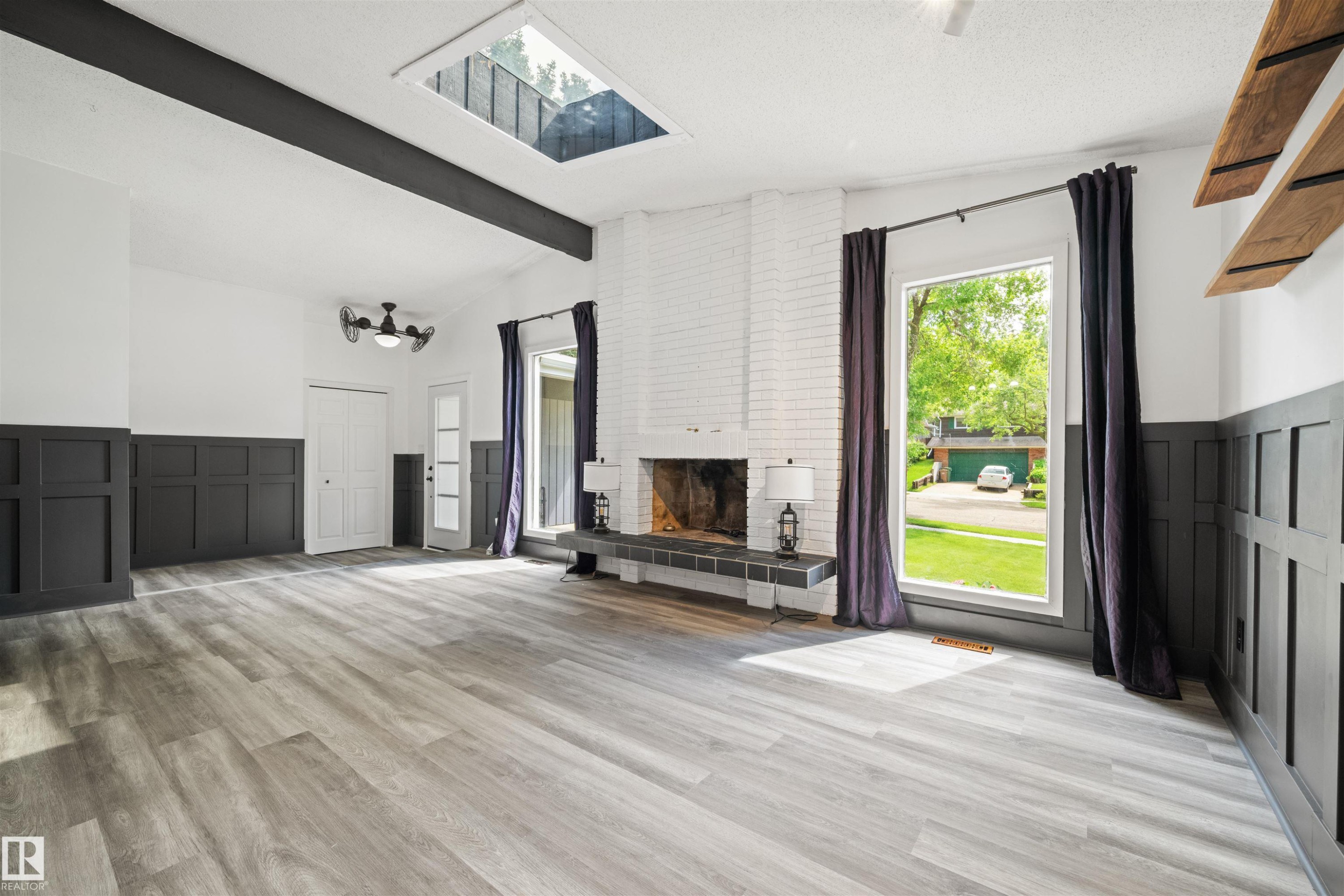 Spacious room featuring wood-finish flooring, a brick fireplace with a tile hearth, and a skylight - 28 Goodridge Drive, St. Albert, AB
