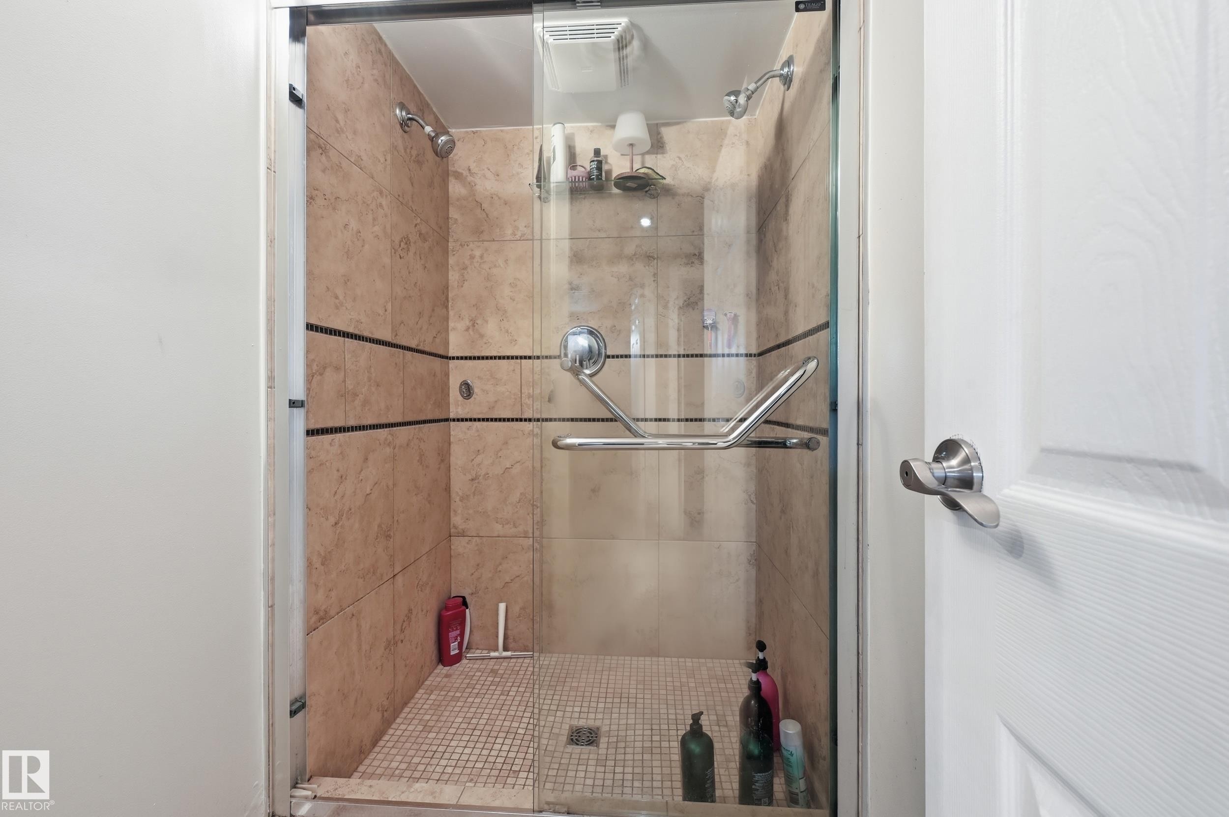 Walk-in shower featuring glass enclosure, stone-look tile surround with decorative accent bands, dual shower heads, and an accessible grab bar - 12326 92 Street, Edmonton, AB - Indoor Photo Showing Bathroom