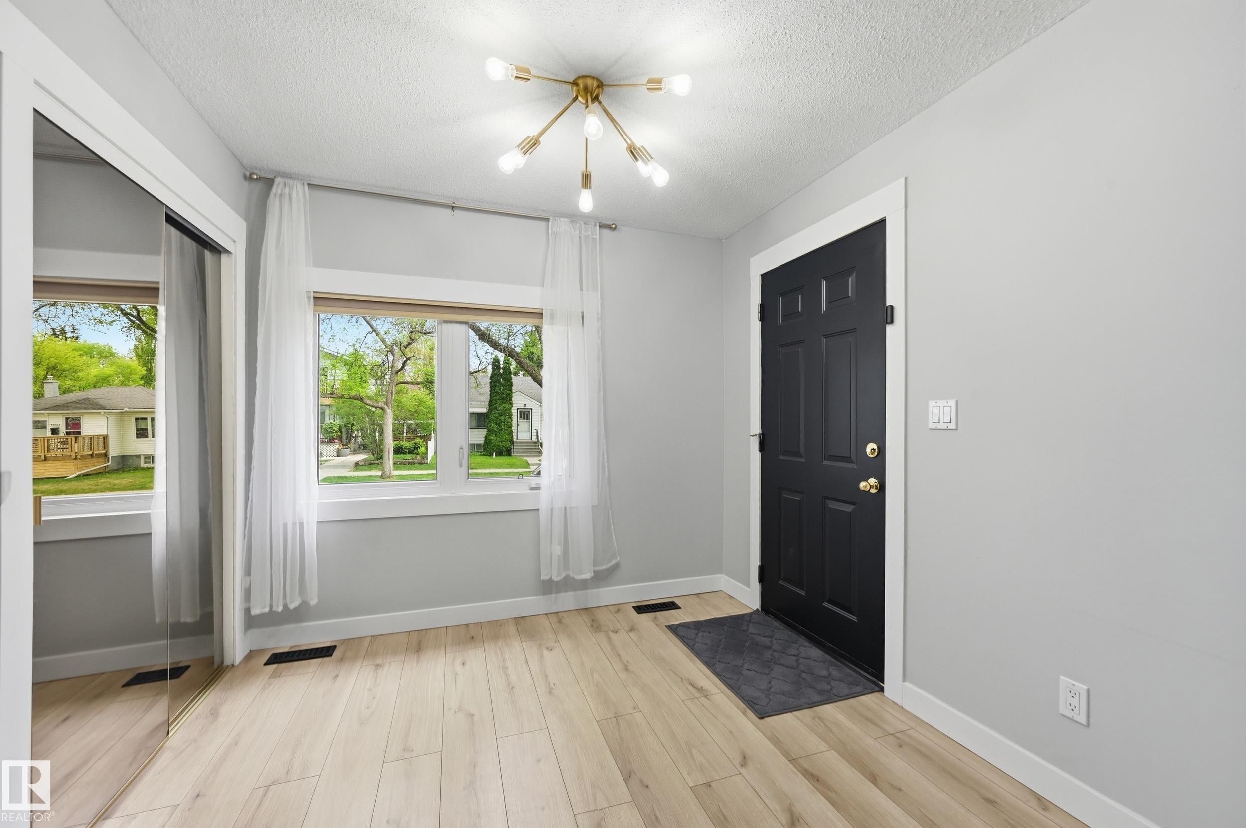 Entry area featuring a dark paneled door with brass hardware, wood-finish flooring, and a modern sputnik-style ceiling light - 12326 92 Street, Edmonton, AB - Indoor Photo Showing Other Room