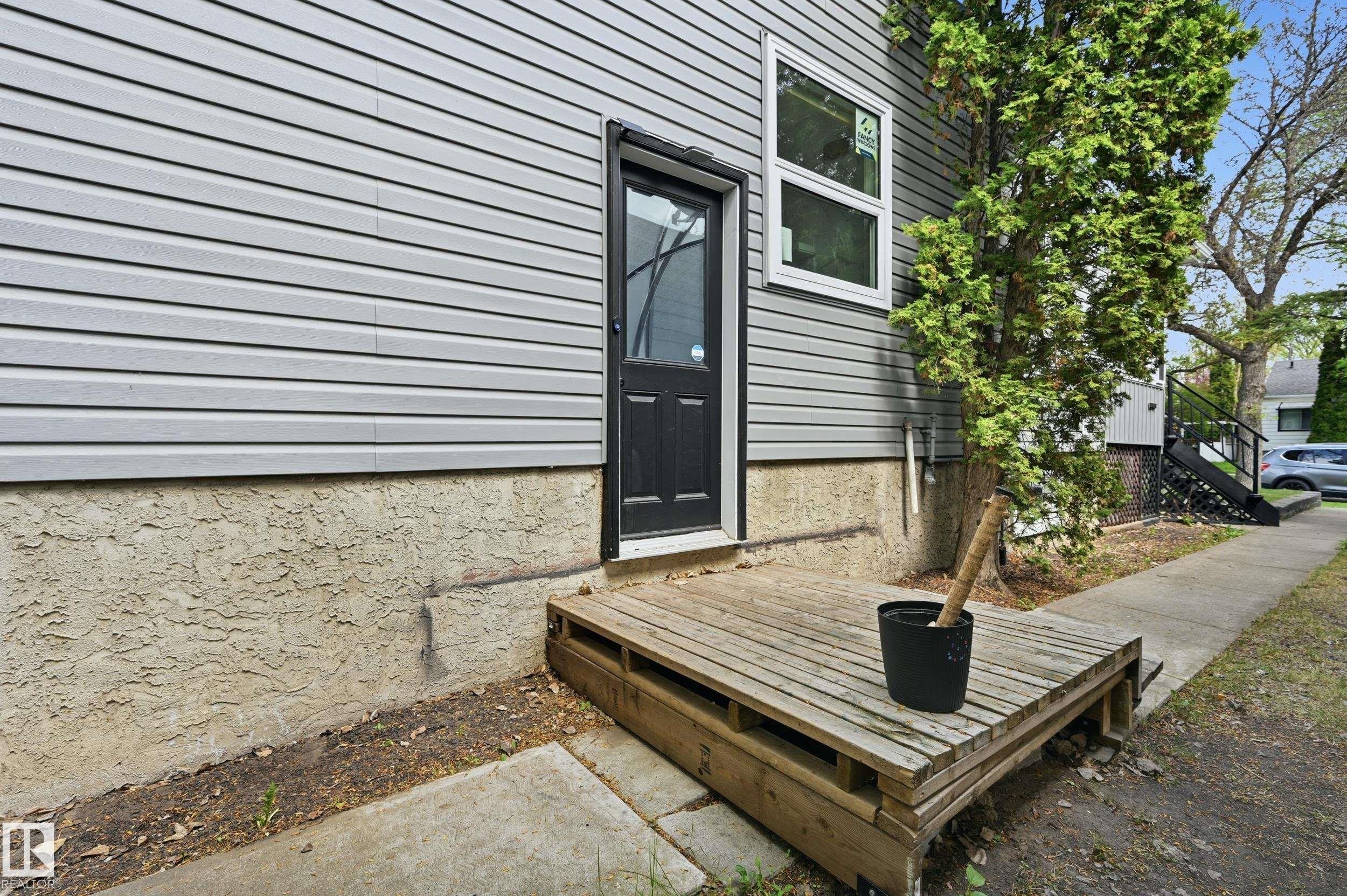 Exterior side entrance featuring a wooden deck, vinyl siding, stucco foundation, and a mature tree - 12326 92 Street, Edmonton, AB - Outdoor With Exterior