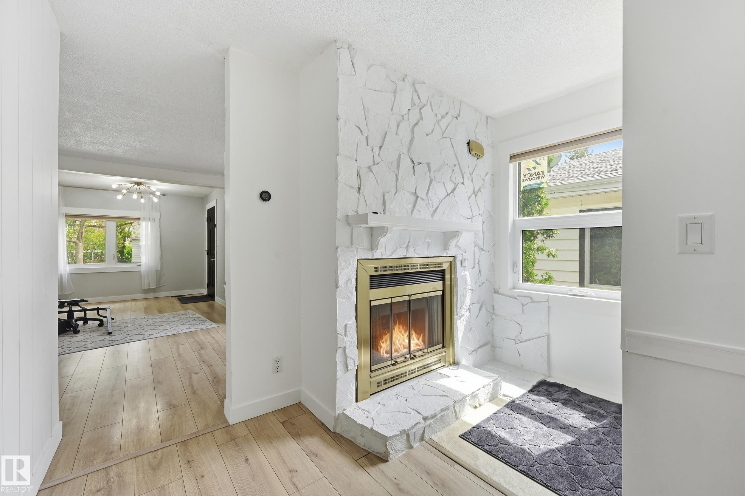 Stone-clad fireplace with a brass-trimmed insert, complemented by light wood-finish flooring - 12326 92 Street, Edmonton, AB - Indoor Photo Showing Other Room With Fireplace