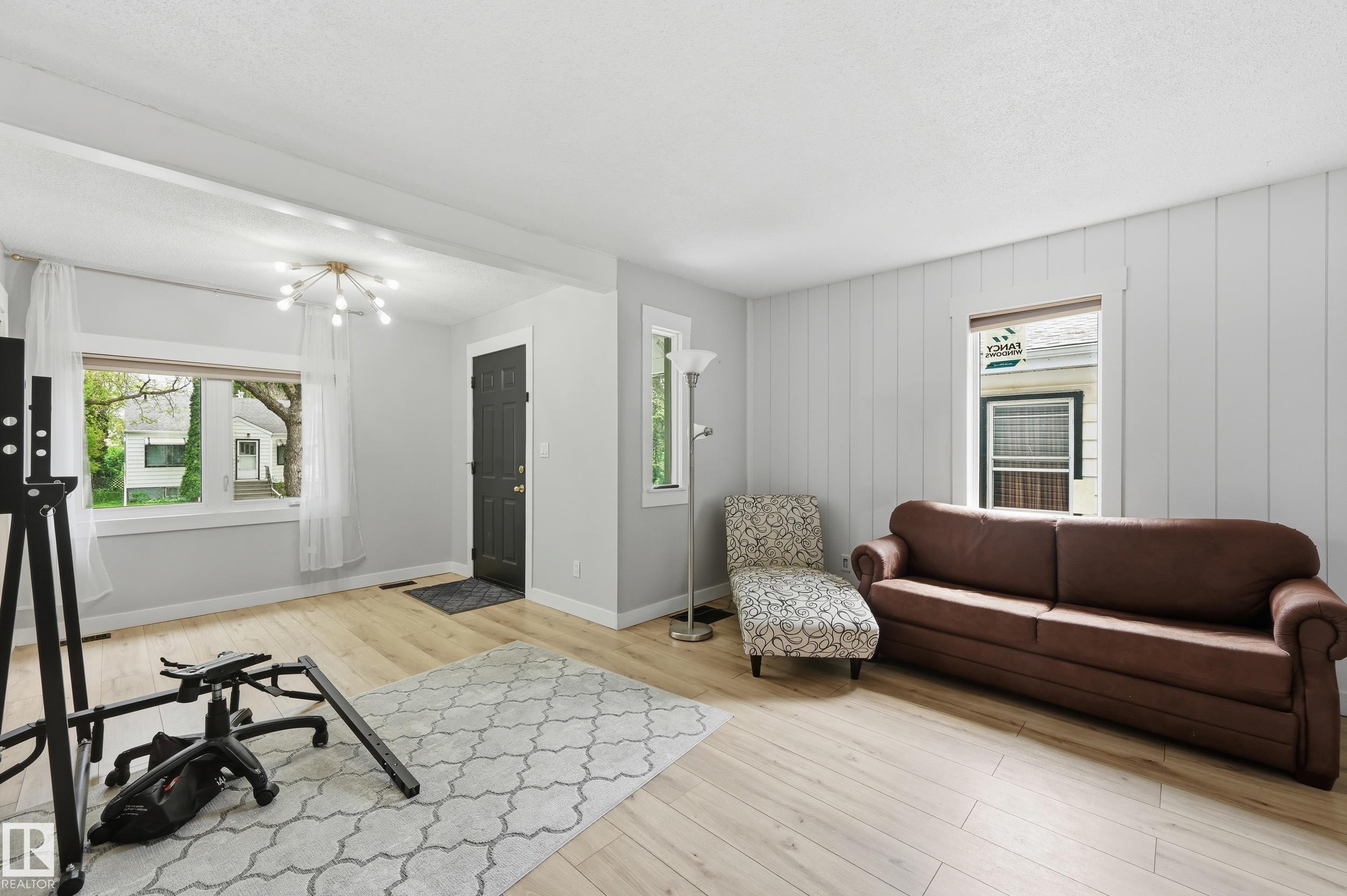 Spacious room featuring light wood-finish flooring, a modern sputnik chandelier, and a dark entry door - 12326 92 Street, Edmonton, AB - Indoor Photo Showing Other Room