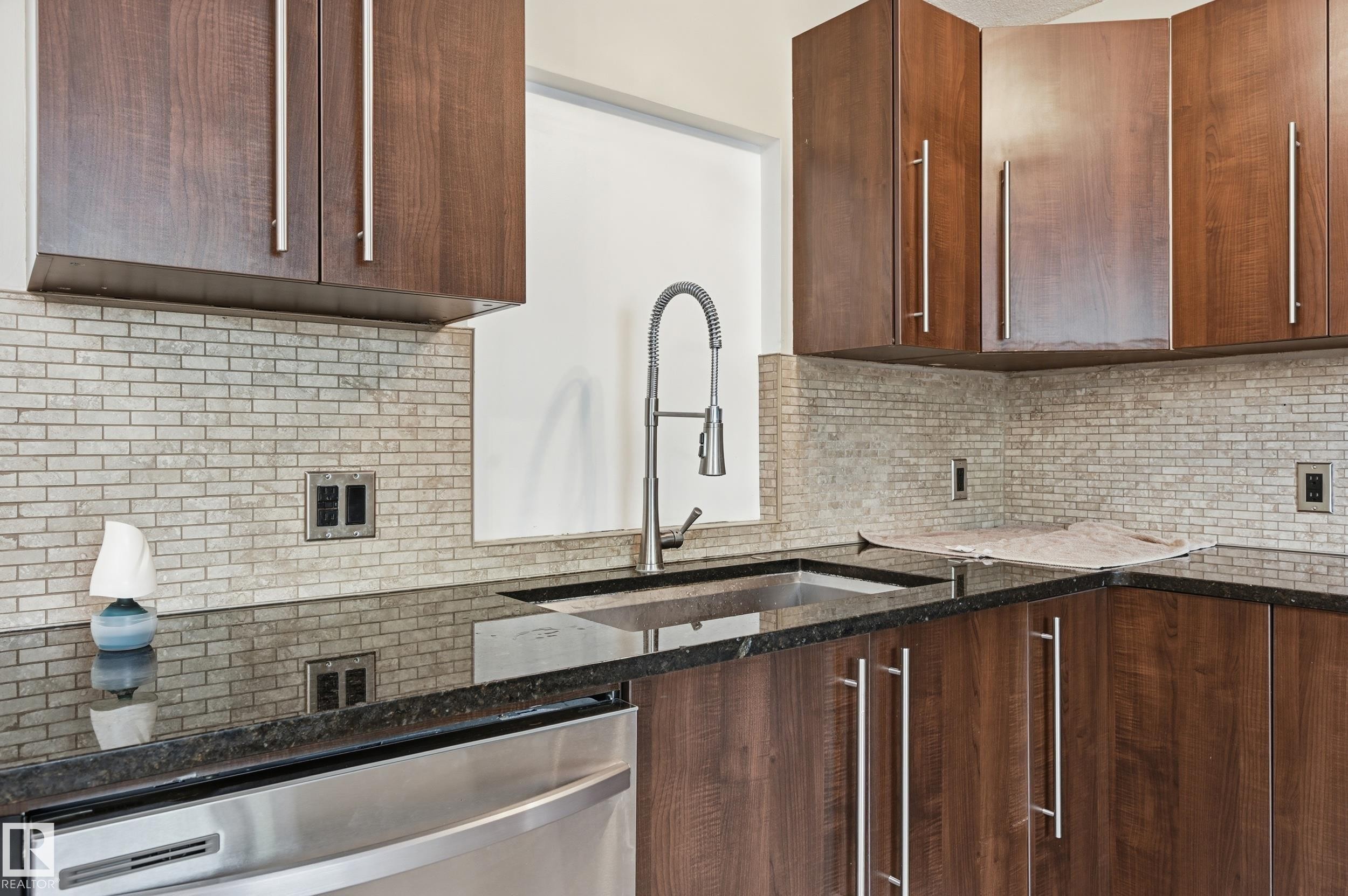 Kitchen featuring dark wood-finish cabinetry with stainless steel pulls, a dark countertop, a stainless steel sink with a gooseneck faucet, a light brick-patterned backsplash, and a stainless steel appliance - 12326 92 Street, Edmonton, AB - Indoor Photo Showing Kitchen With Upgraded Kitchen