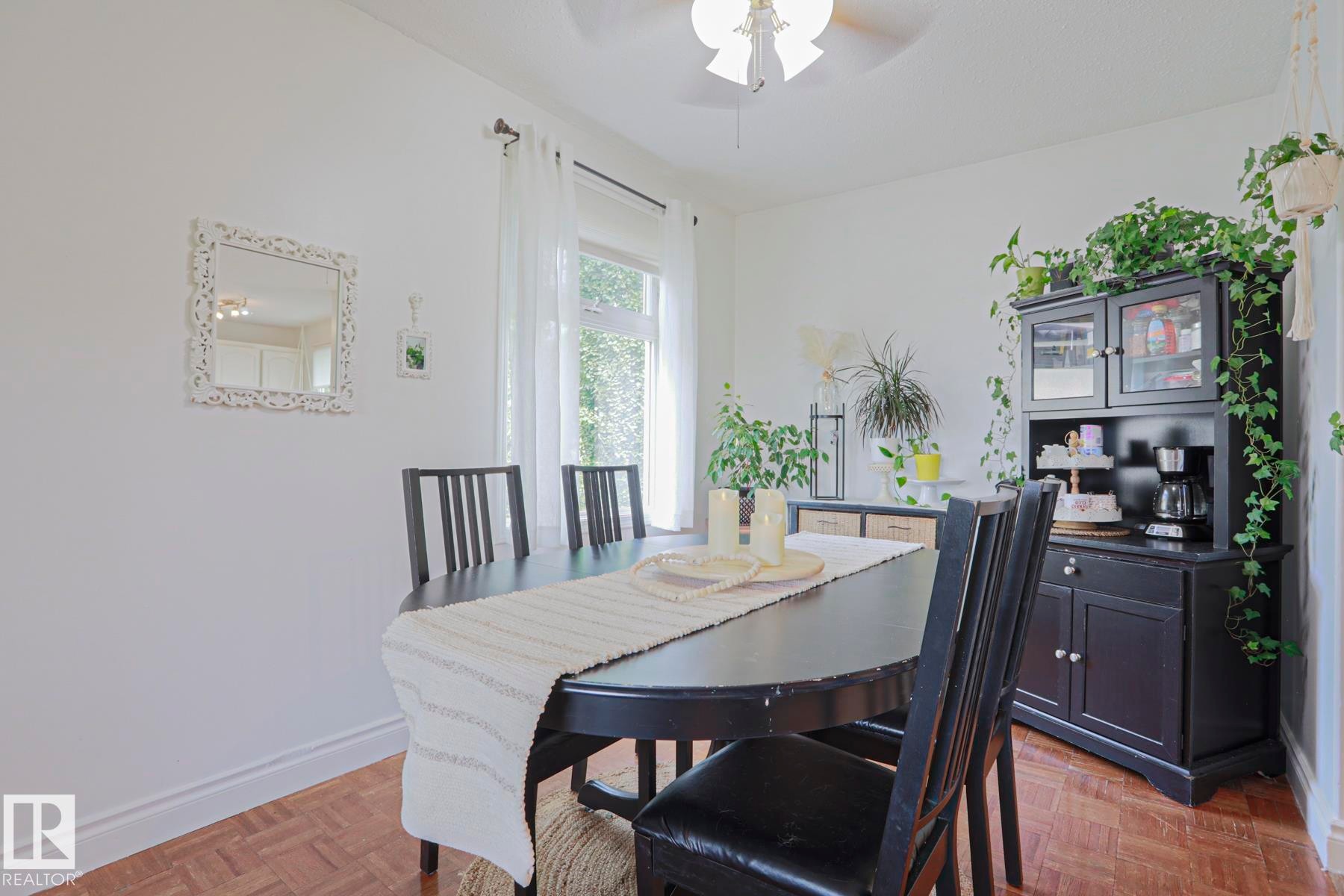 Spacious dining area featuring wood-finish flooring, white baseboards, and a large window with sheer drapery - 2007 67 Street, Edmonton, AB
