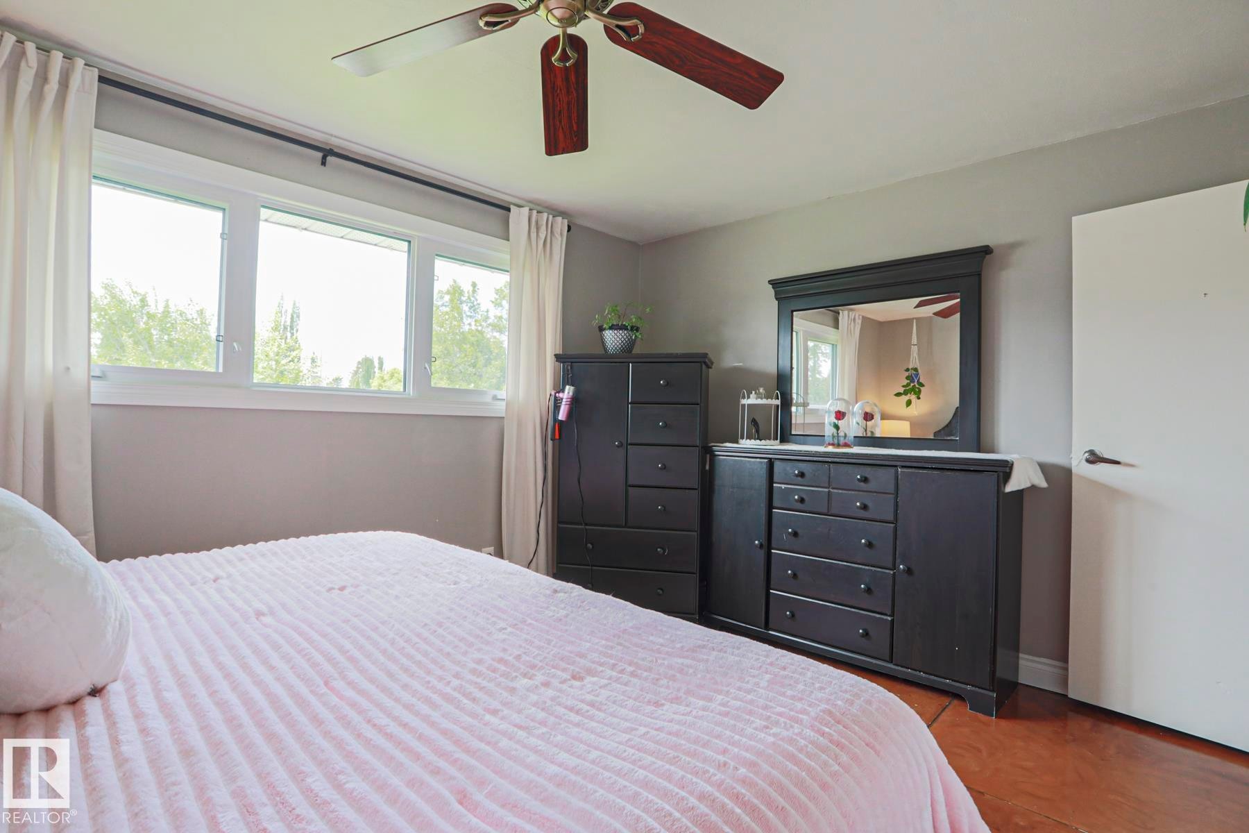 Bedroom featuring light gray walls, wood-finish flooring, and a ceiling fan with wood-tone blades - 2007 67 Street, Edmonton, AB