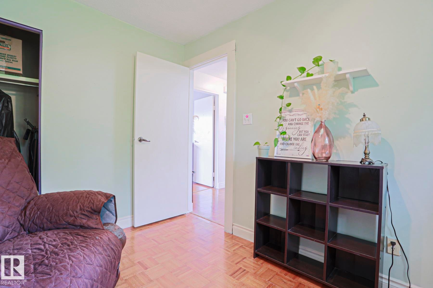 Interior room featuring parquet wood flooring, light green wall paint, a white interior door, and a built-in closet with dark shelving - 2007 67 Street, Edmonton, AB