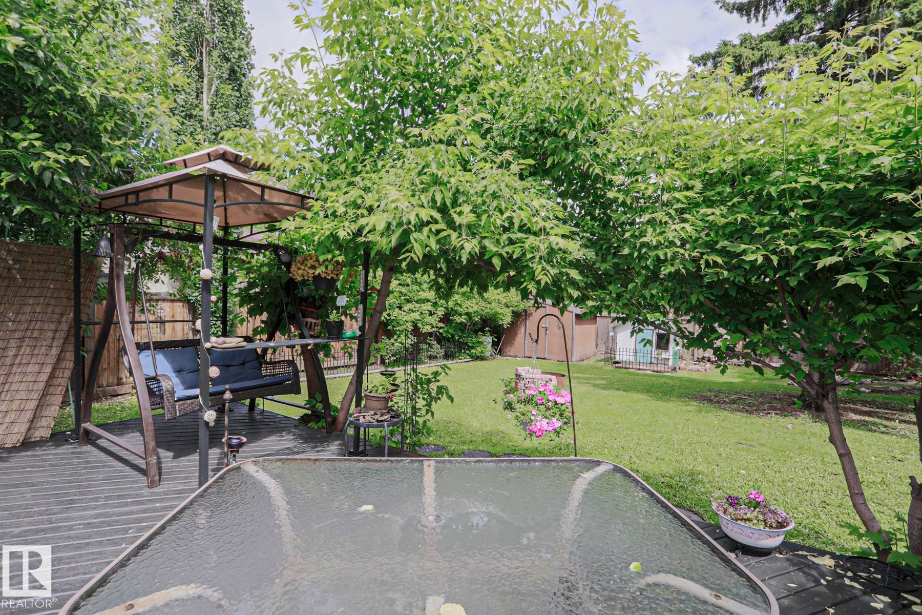 Expansive backyard featuring a lush lawn, mature trees, and a dark-toned deck - 2007 67 Street, Edmonton, AB
