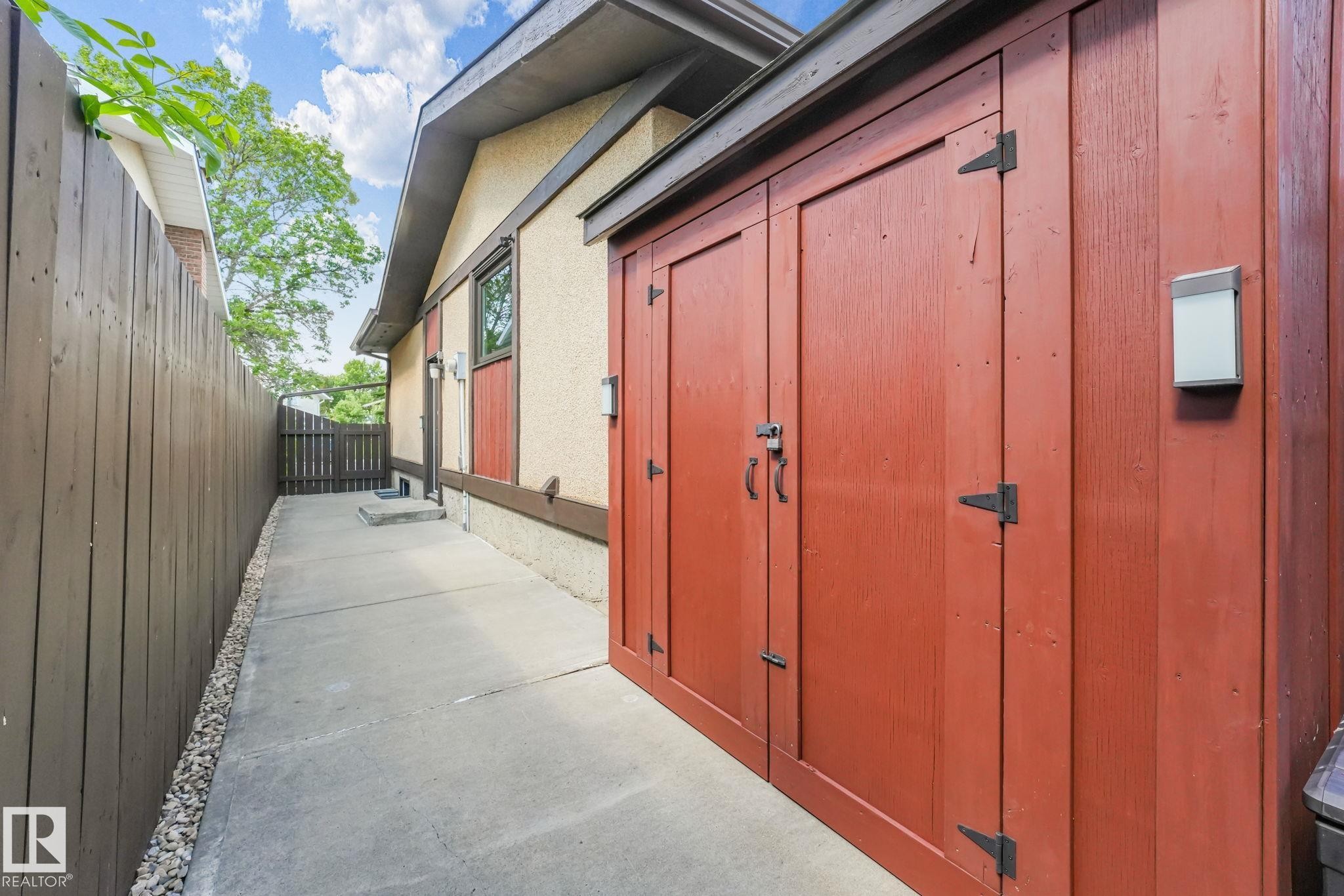 Red-stained wood storage shed featuring black metal hardware, positioned on a concrete pathway - 17237 104 Street, Edmonton, AB