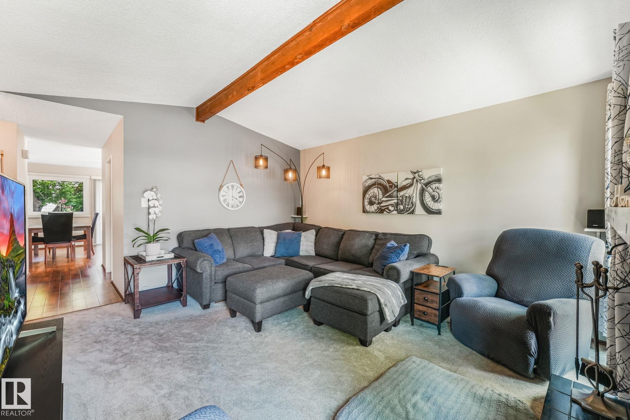 Living room featuring a vaulted ceiling with exposed wood beam, light grey wall tones, and neutral carpet flooring - 17237 104 Street, Edmonton, AB