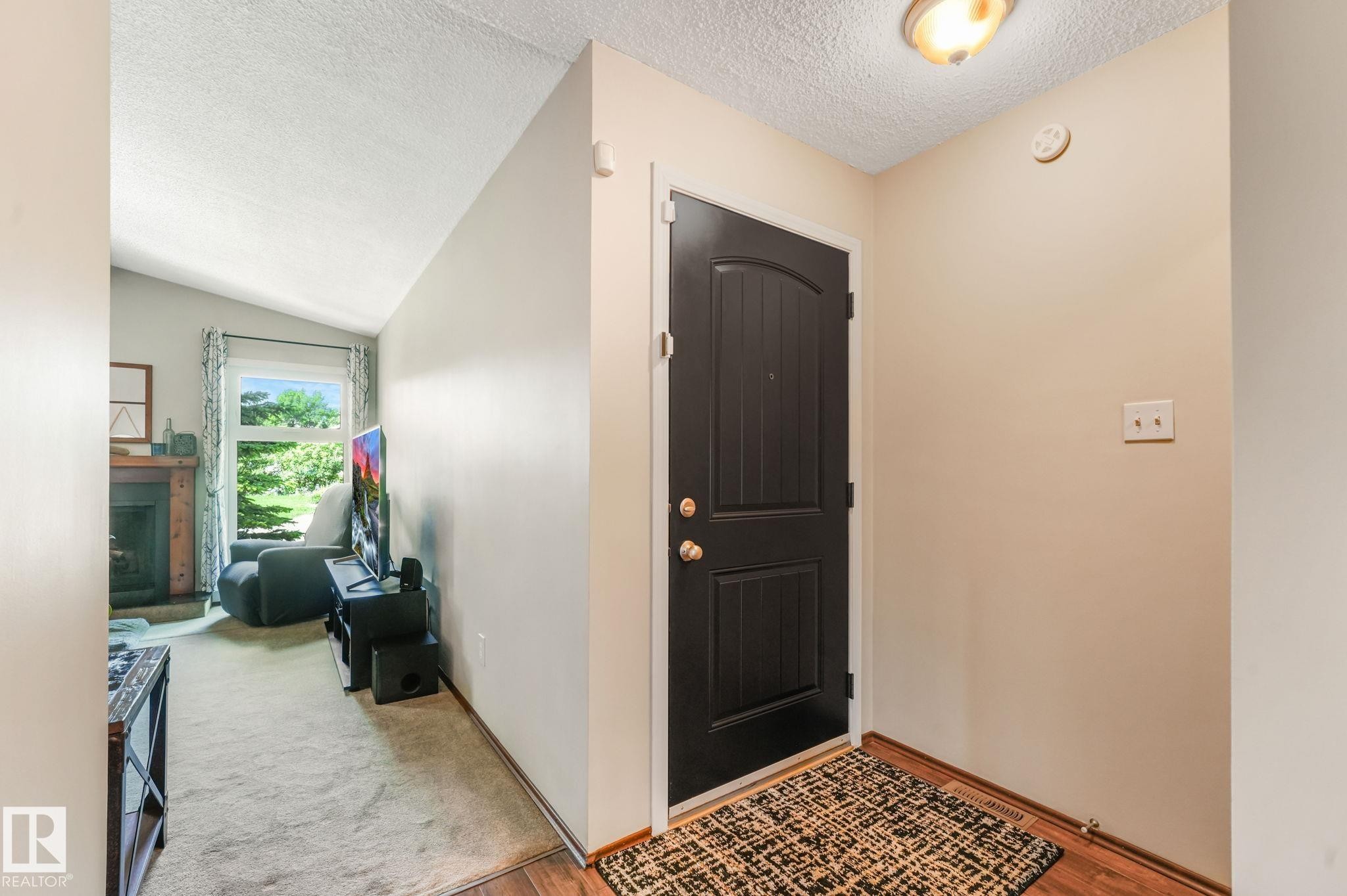 Entryway featuring a dark paneled door with brass hardware, wood-finish flooring, and a flush mount ceiling light - 17237 104 Street, Edmonton, AB