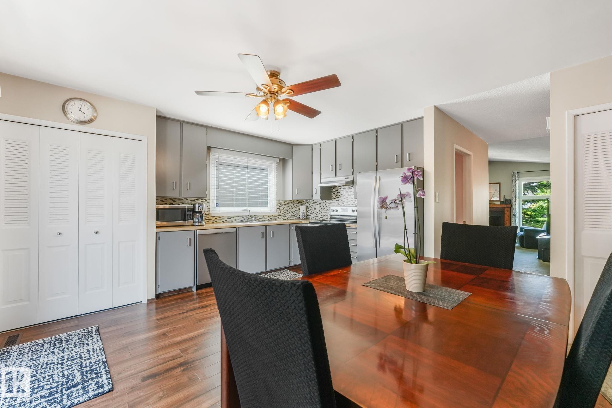 Open-concept living area featuring wood-finish flooring, a contemporary ceiling fan, and a kitchen with gray cabinetry, a tile backsplash, and stainless steel appliances - 17237 104 Street, Edmonton, AB