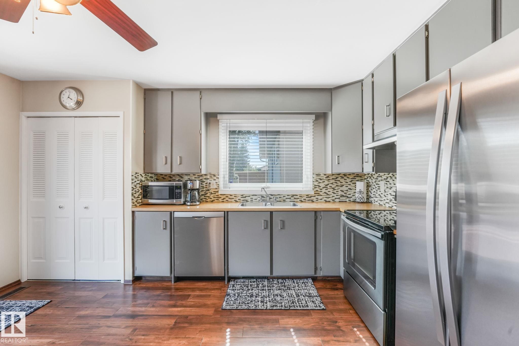 Kitchen featuring wood-finish flooring, gray cabinetry, stainless steel appliances, and a mosaic tile backsplash - 17237 104 Street, Edmonton, AB