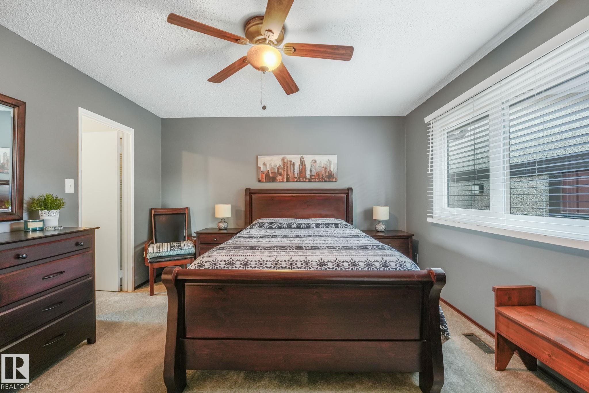 Spacious bedroom featuring neutral wall tones, textured ceiling, a ceiling fan with integrated lighting, a large window with blinds, and carpeted flooring - 17237 104 Street, Edmonton, AB