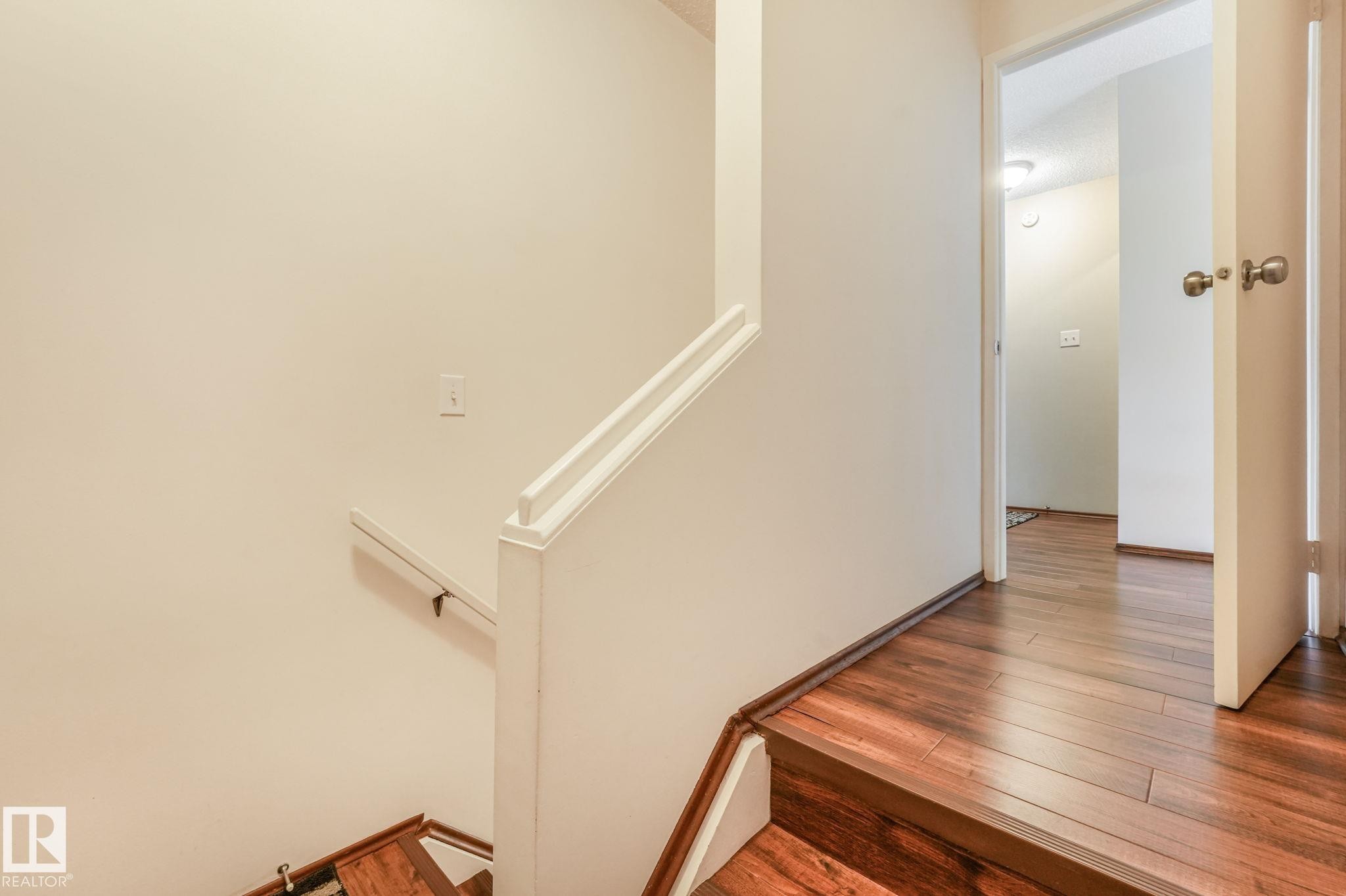 Staircase featuring wood-finish flooring, a white painted handrail, and light neutral wall finishes - 17237 104 Street, Edmonton, AB