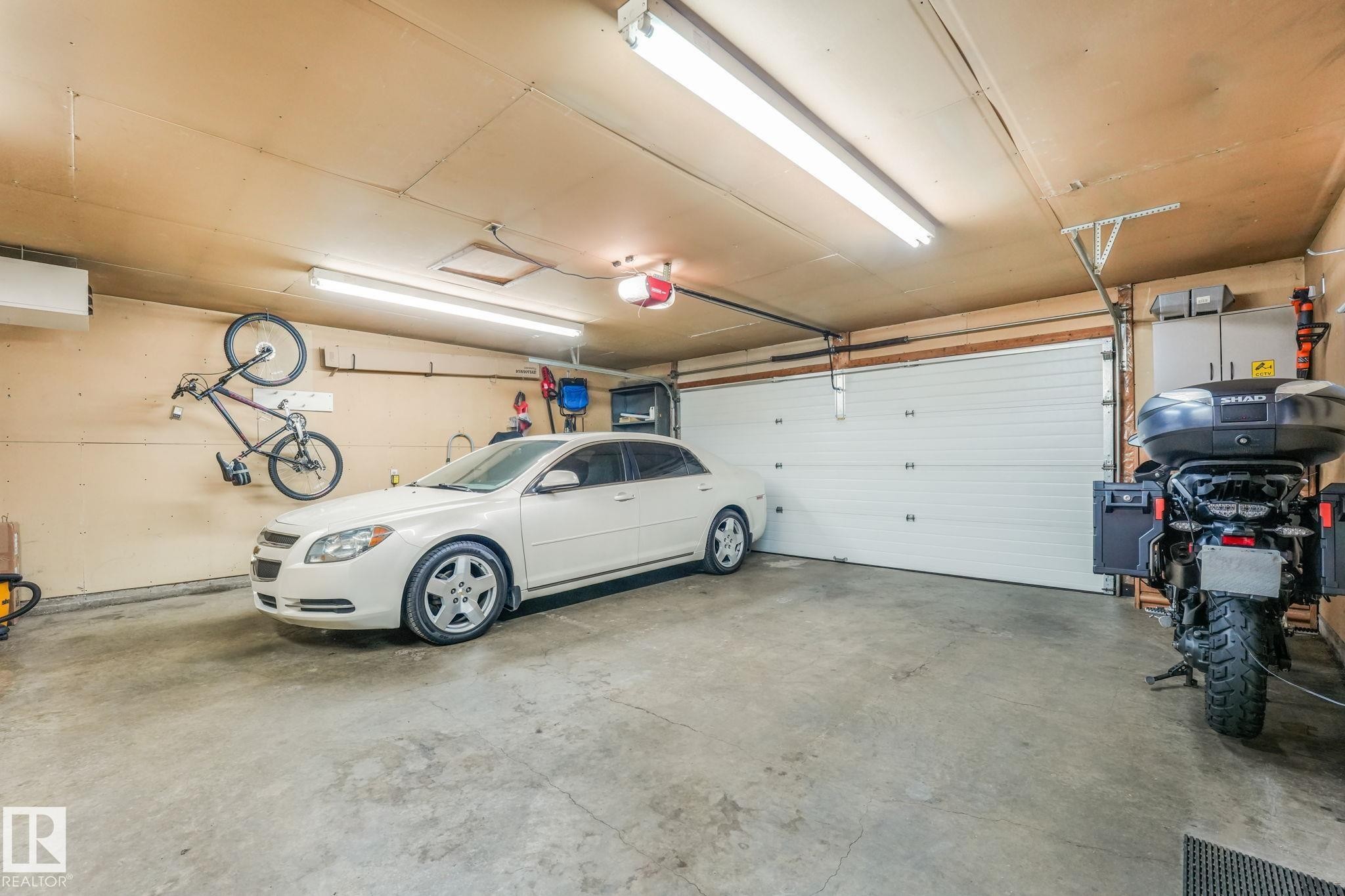 Attached garage featuring a white sectional garage door, concrete flooring, and overhead fluorescent lighting - 17237 104 Street, Edmonton, AB