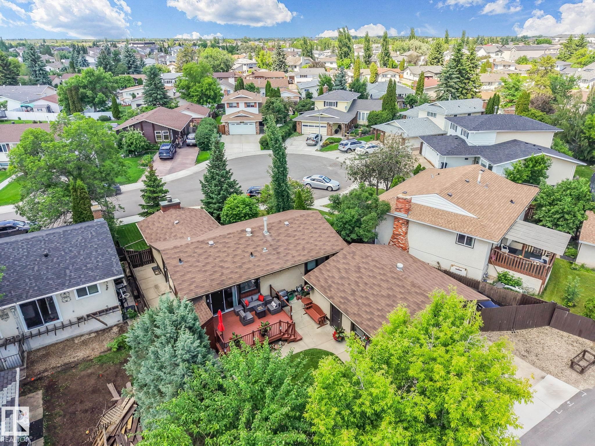 Expansive rear deck featuring a red umbrella, multiple seating arrangements, and direct access to the interior via a sliding glass door - 17237 104 Street, Edmonton, AB