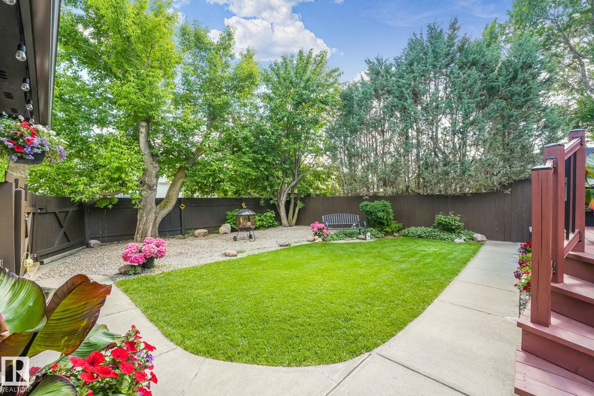 Expansive backyard featuring a lush lawn, concrete pathway, mature trees, and a privacy fence - 17237 104 Street, Edmonton, AB