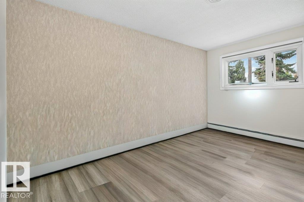 Room featuring wood-finish flooring, white baseboards, and a textured accent wall - 6916 92A Avenue, Edmonton, AB