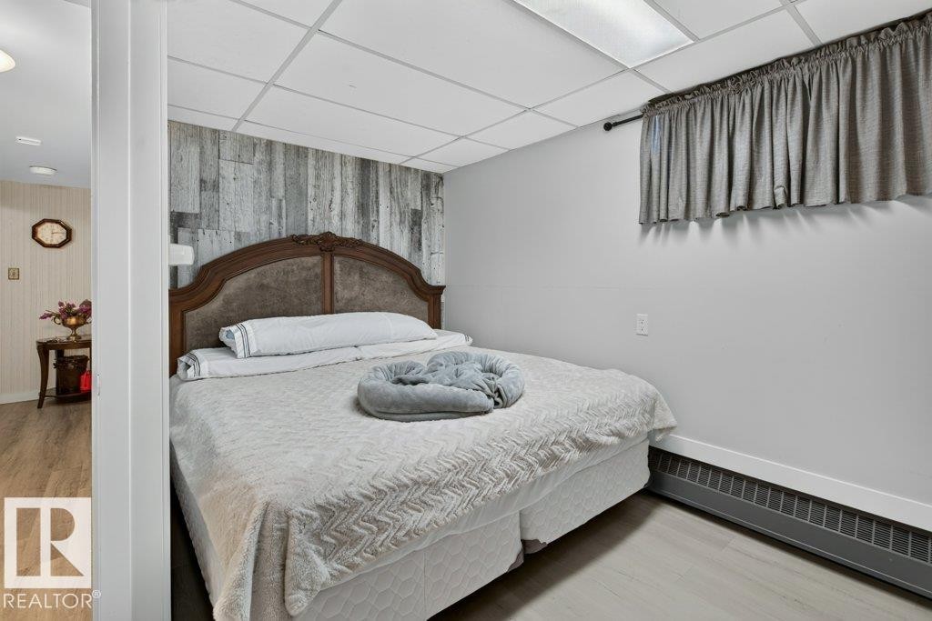 Bedroom featuring a decorative wood-finish accent wall, light grey walls, and light wood-look flooring - 6916 92A Avenue, Edmonton, AB
