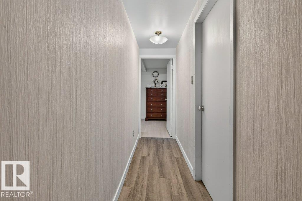 Hallway featuring wood-finish flooring, textured wall coverings, a ceiling-mounted light fixture, and white interior doors with round knobs - 6916 92A Avenue, Edmonton, AB