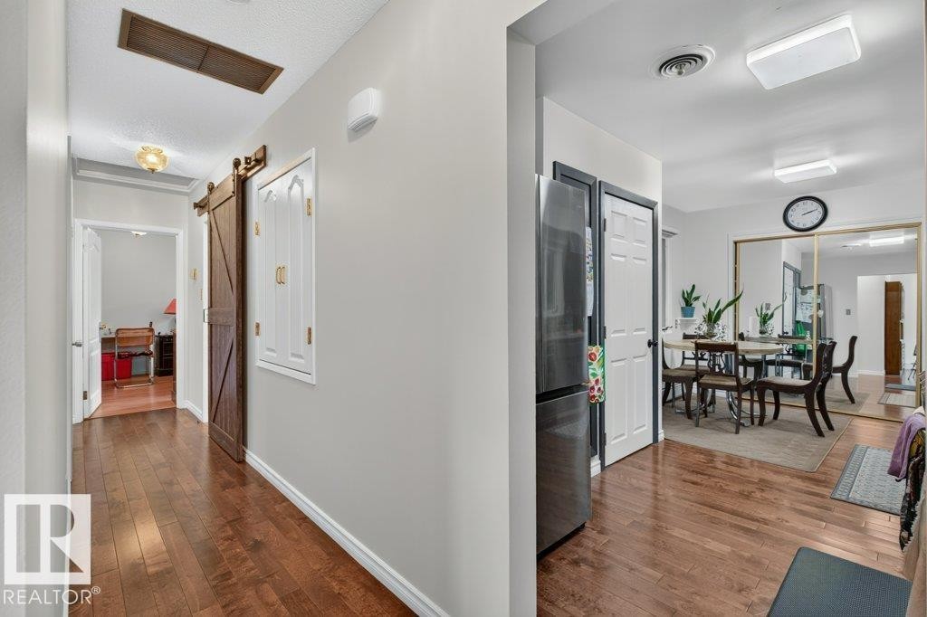 Hallway featuring rich wood-finish flooring, light grey painted walls, a sliding barn door, and recessed ceiling lighting - 6916 92A Avenue, Edmonton, AB