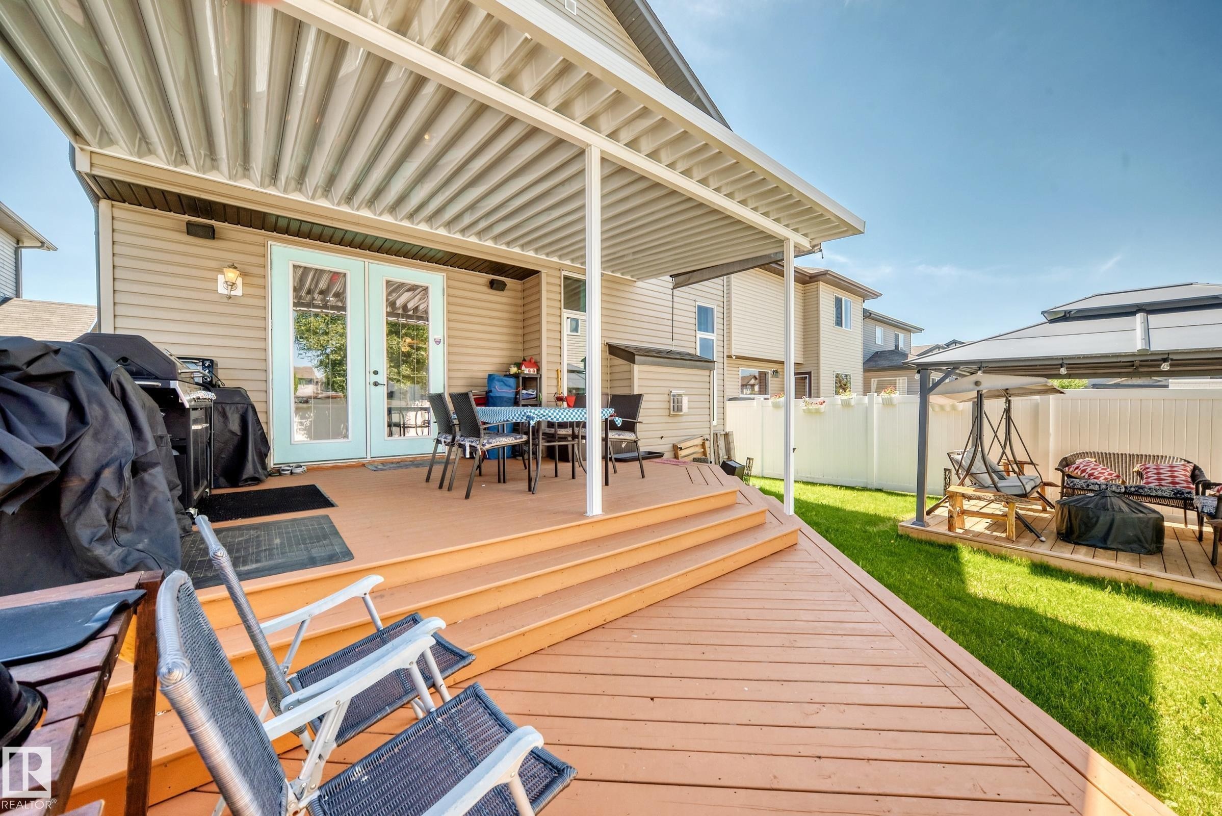 Expansive wood-finish deck with multiple levels, featuring a covered patio area and direct access to the interior via double French doors - 12410 171A Avenue, Edmonton, AB