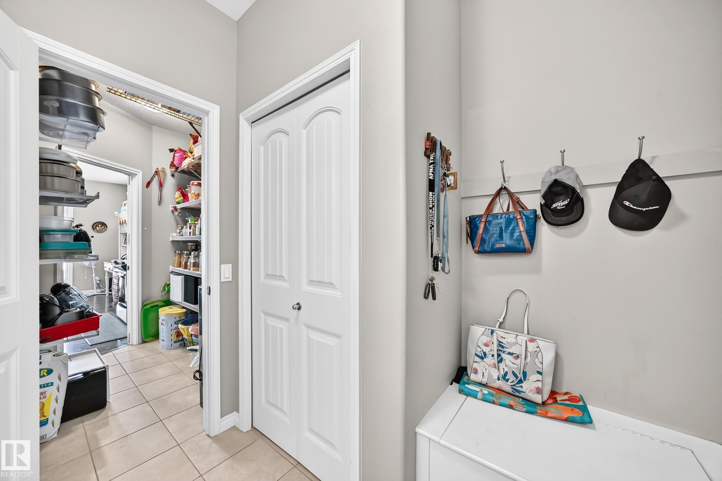 Utility area featuring light-toned tile flooring, a double-door closet with arch-top panels, and an open doorway revealing additional storage - 12410 171A Avenue, Edmonton, AB