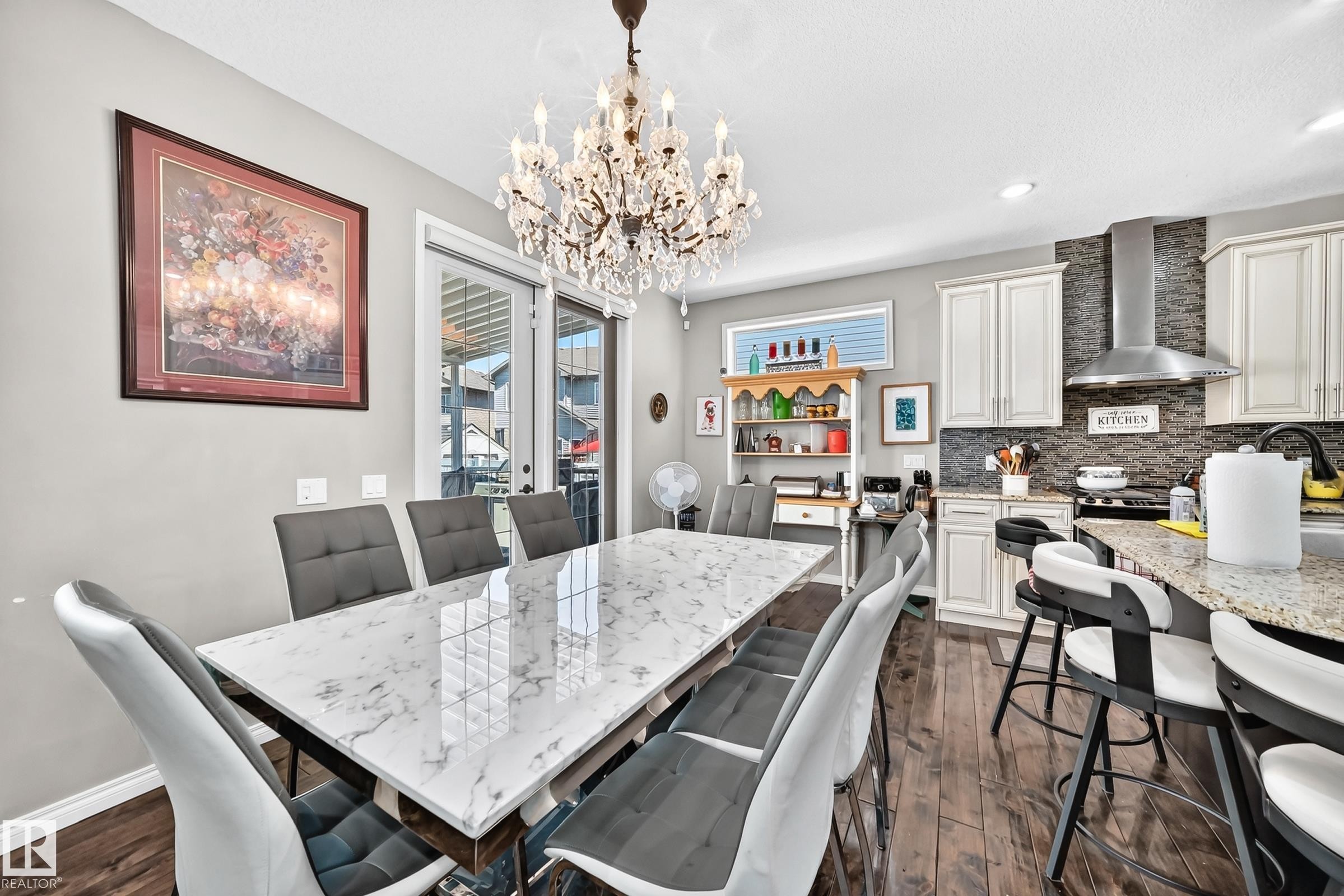 Open-concept dining and kitchen area featuring a crystal chandelier, wood-finish flooring, and white cabinetry - 12410 171A Avenue, Edmonton, AB