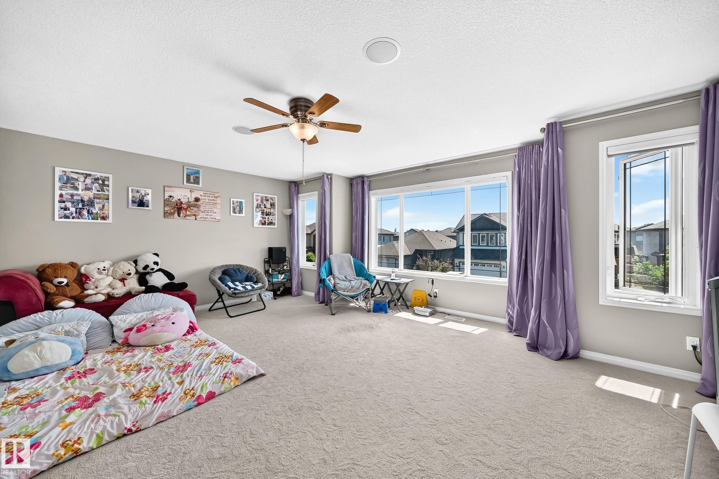 Spacious room featuring light gray wall paint, light-colored carpeting, a ceiling fan with light fixture, and multiple windows providing ambient light - 12410 171A Avenue, Edmonton, AB