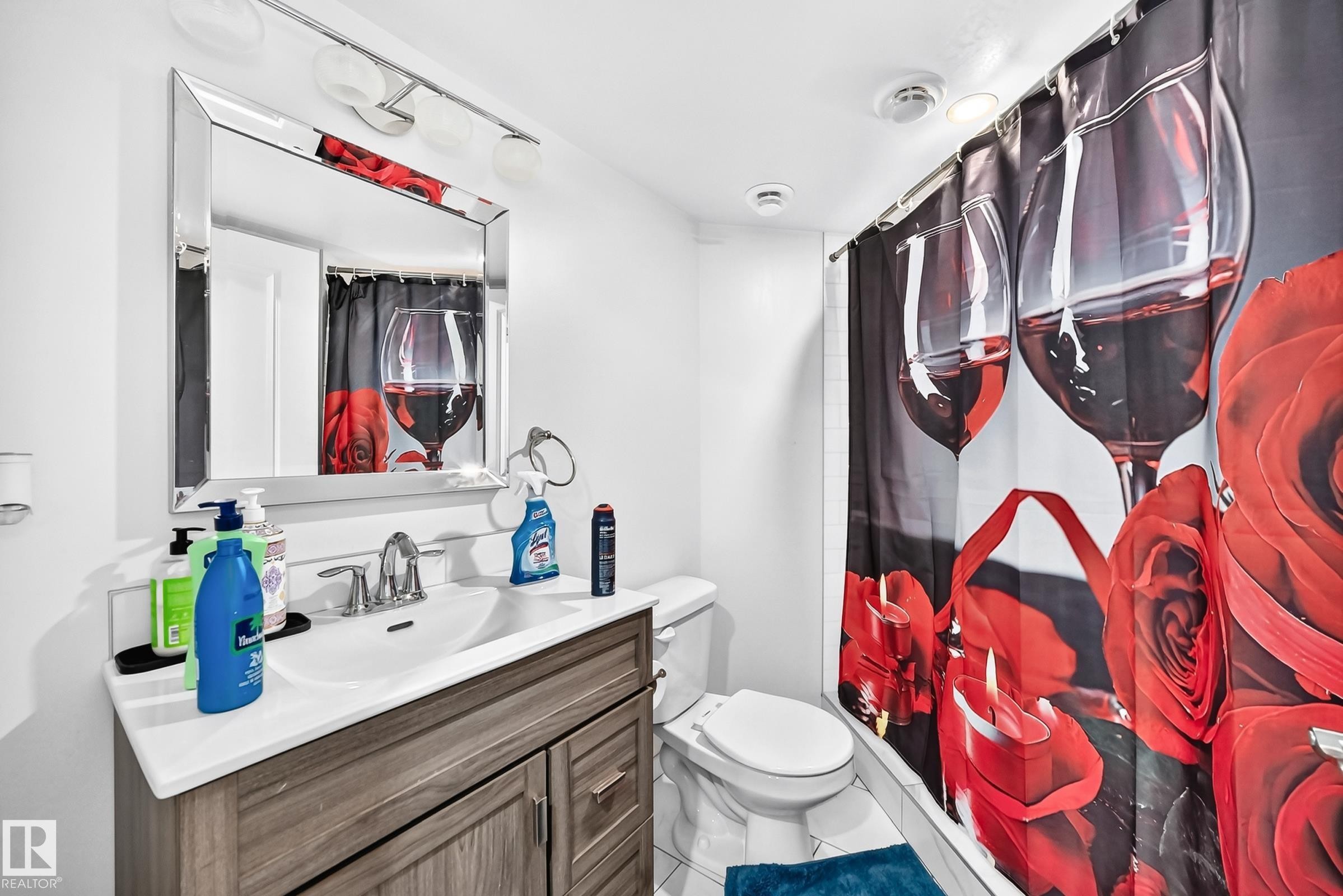 Bathroom featuring a wood-finish vanity with a white countertop and integrated sink, a large wall mirror, and a chrome-finish light fixture with three globe lights - 12410 171A Avenue, Edmonton, AB